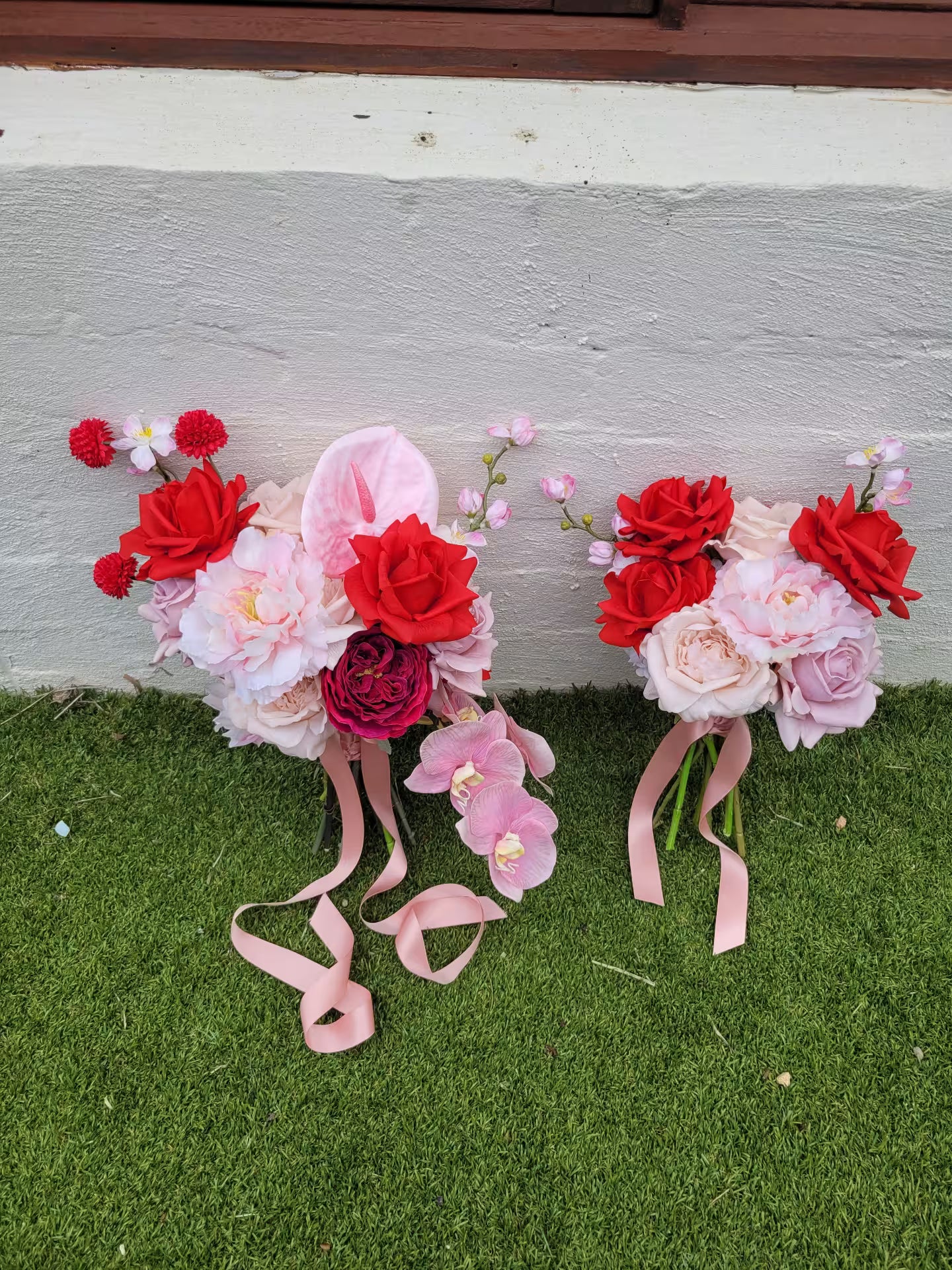 Two wedding bouquets with red and pink flowers on a grassy surface.