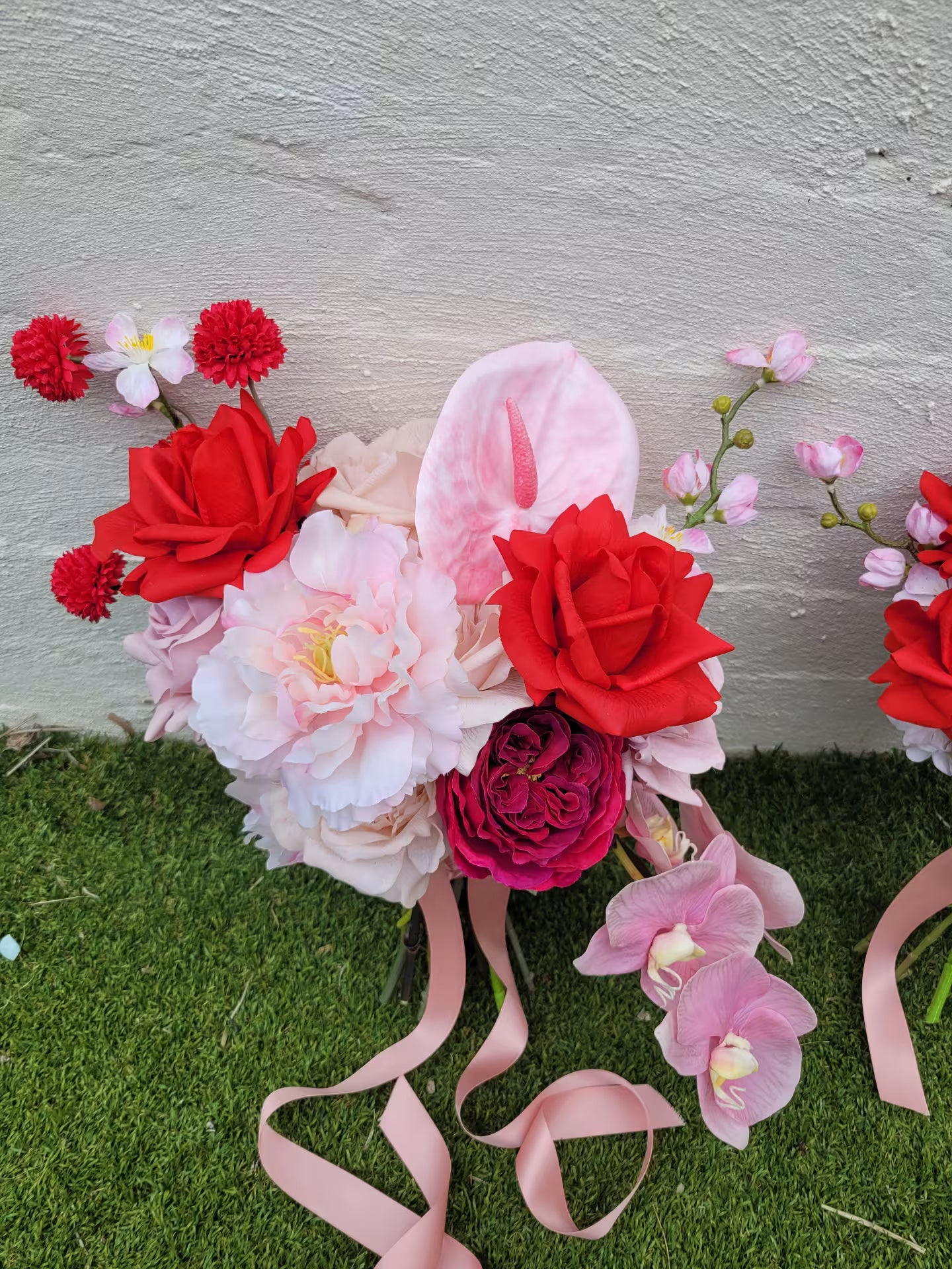 Wedding bouquet with red, pink, and white flowers on a grassy surface.
