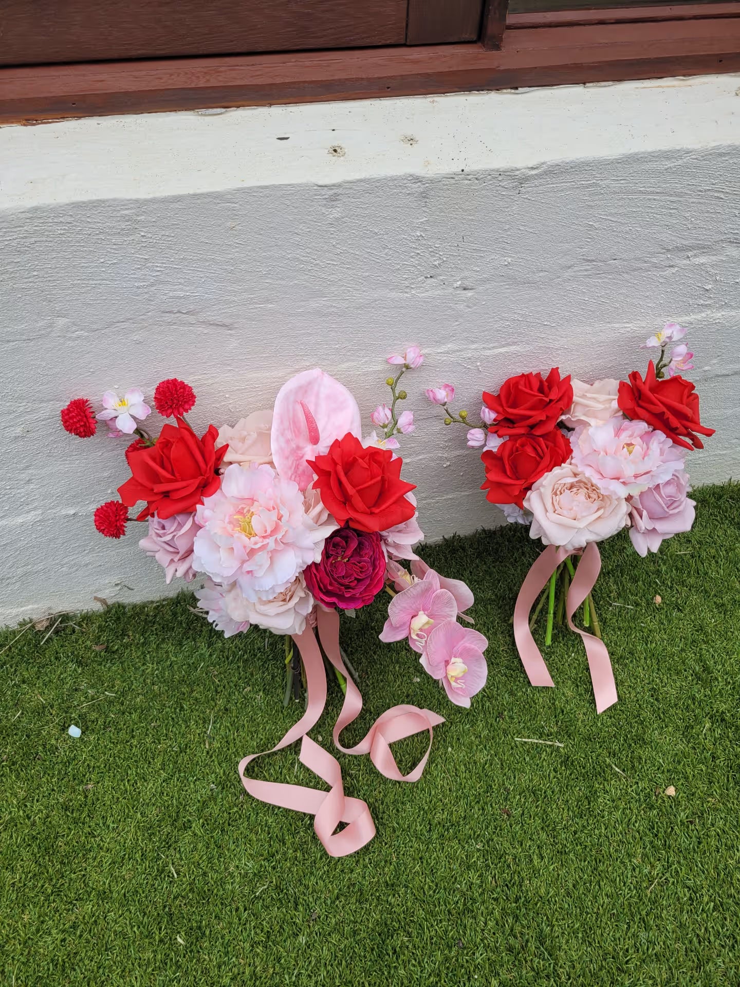 Wedding bouquets with red and pink flowers on a grassy surface.