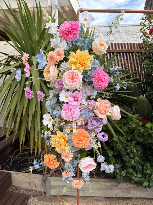 Colorful floral arrangement in a garden setting with plants and a wooden fence.