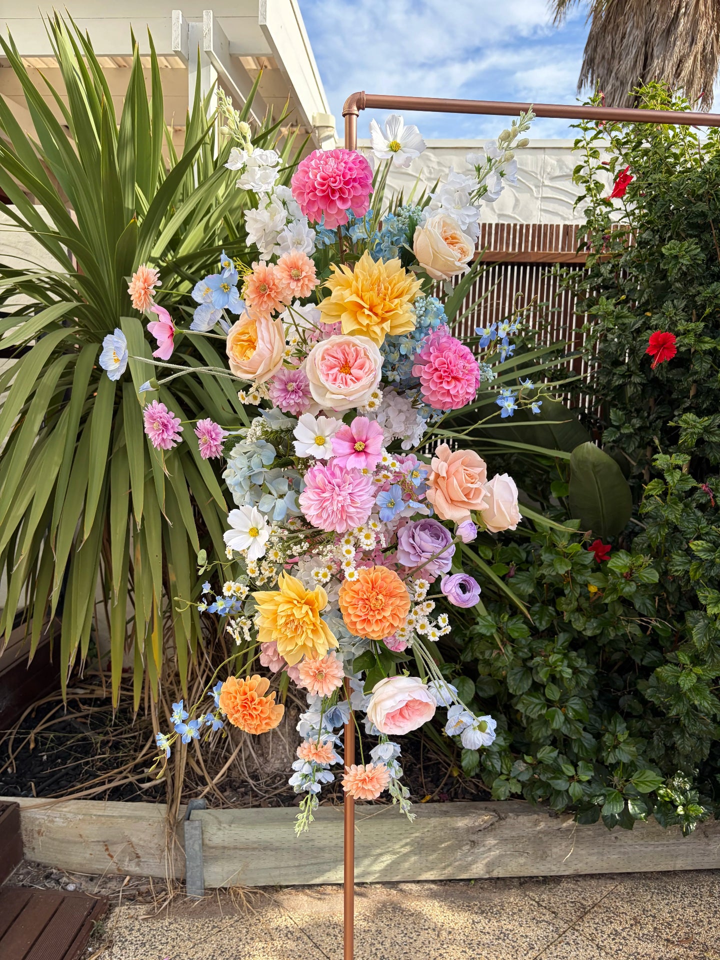 Pastel floral arrangement packed full of spring flowers on a frame in a garden setting