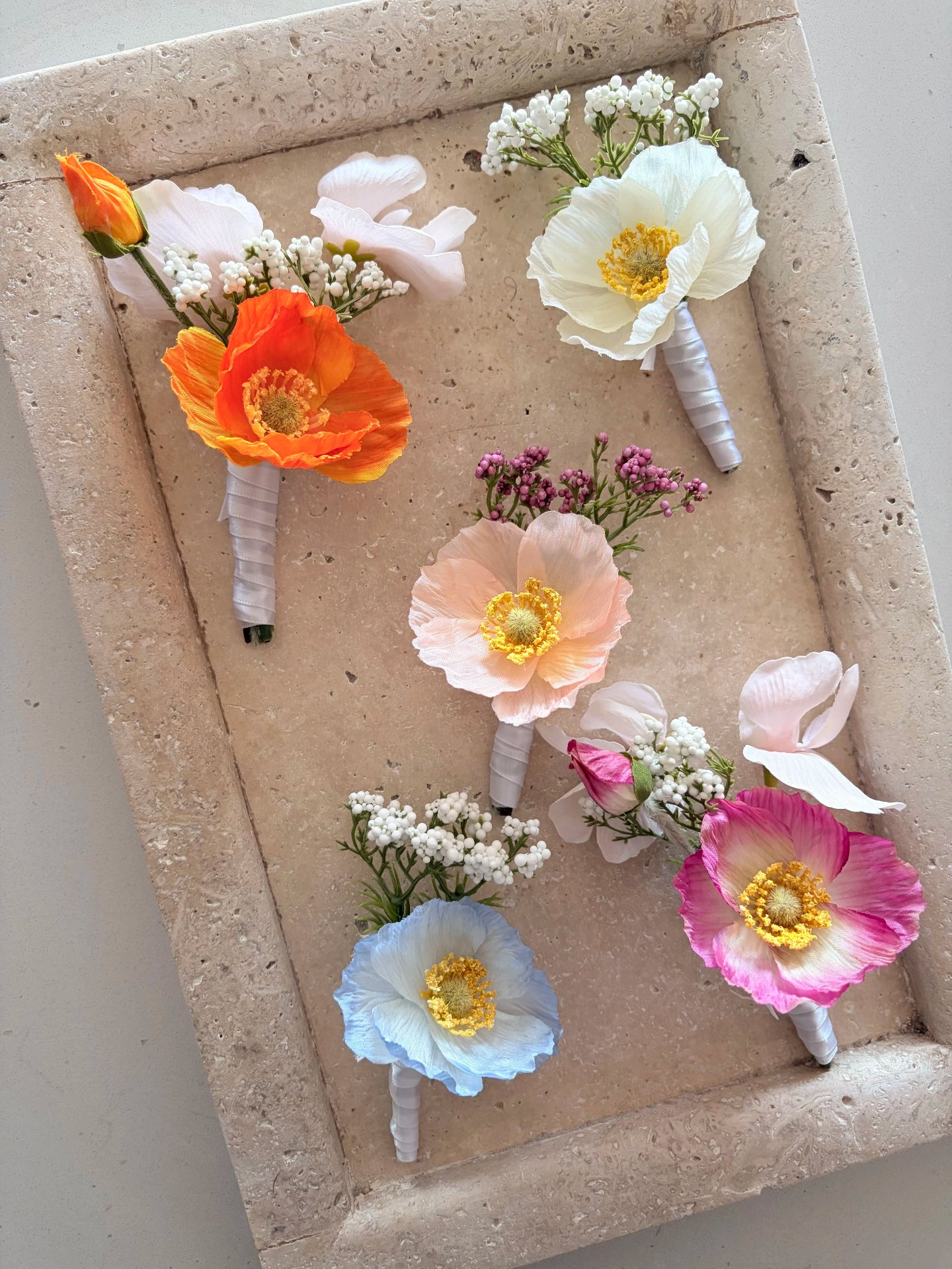 Five buttonholes in orange, white, peach, blue and pink on a travertine tray