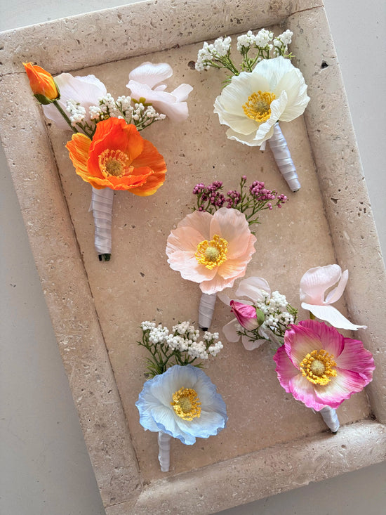 Five buttonholes in orange, white, peach, blue and pink on a travertine tray