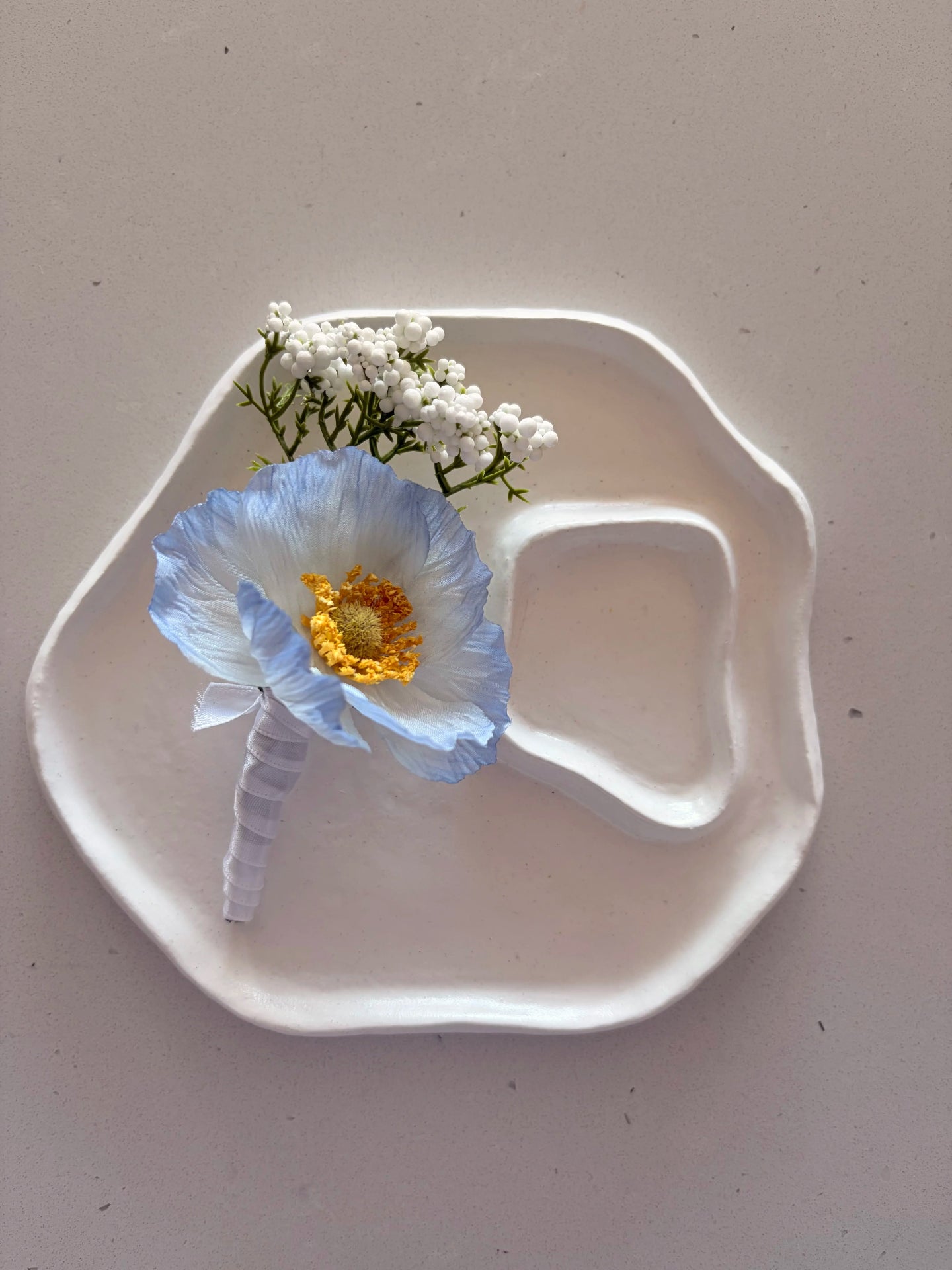 Blue poppy buttonhole on a a small white sculpted plate