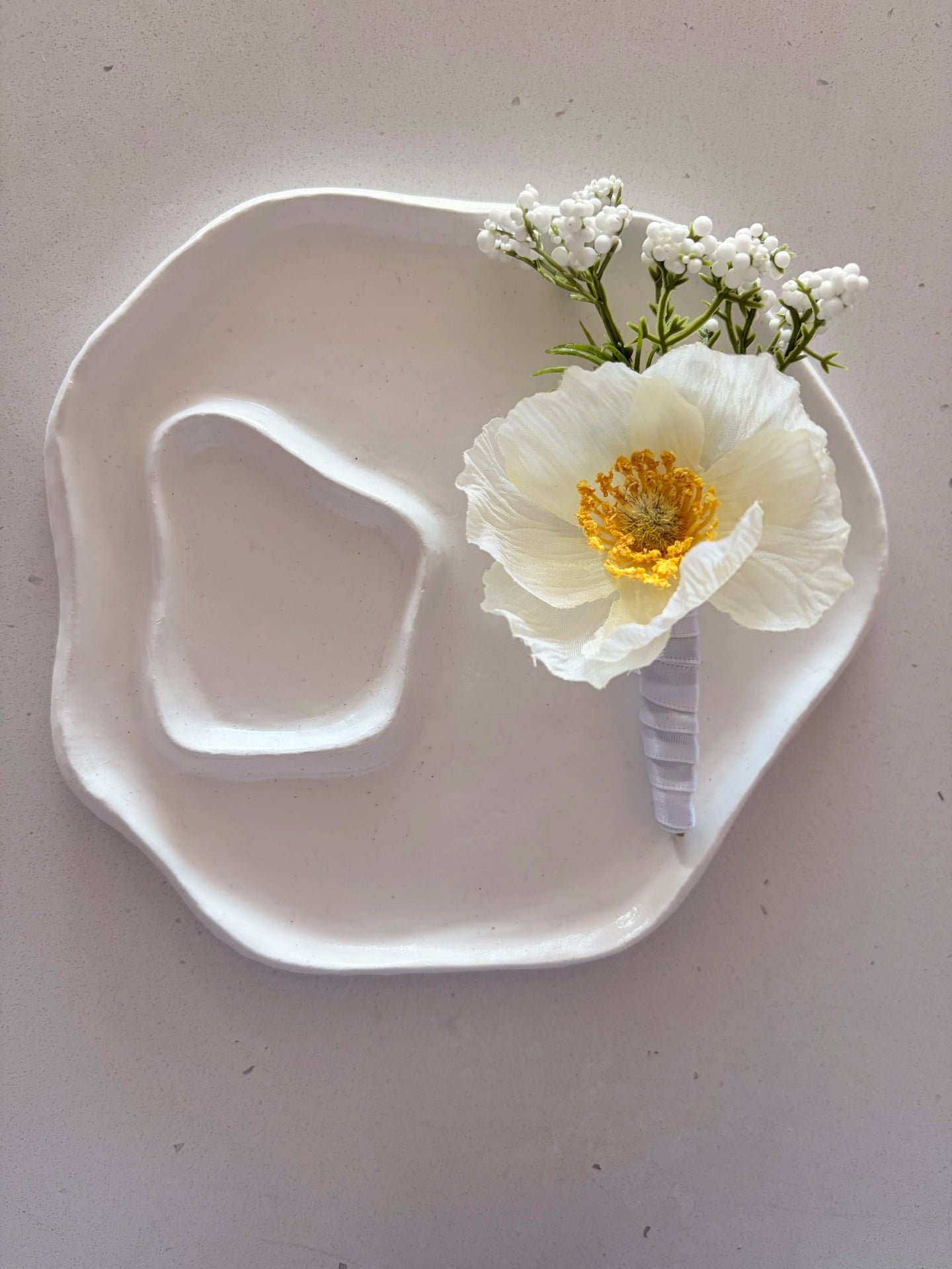 White poppy buttonhole on a a small white sculpted plate