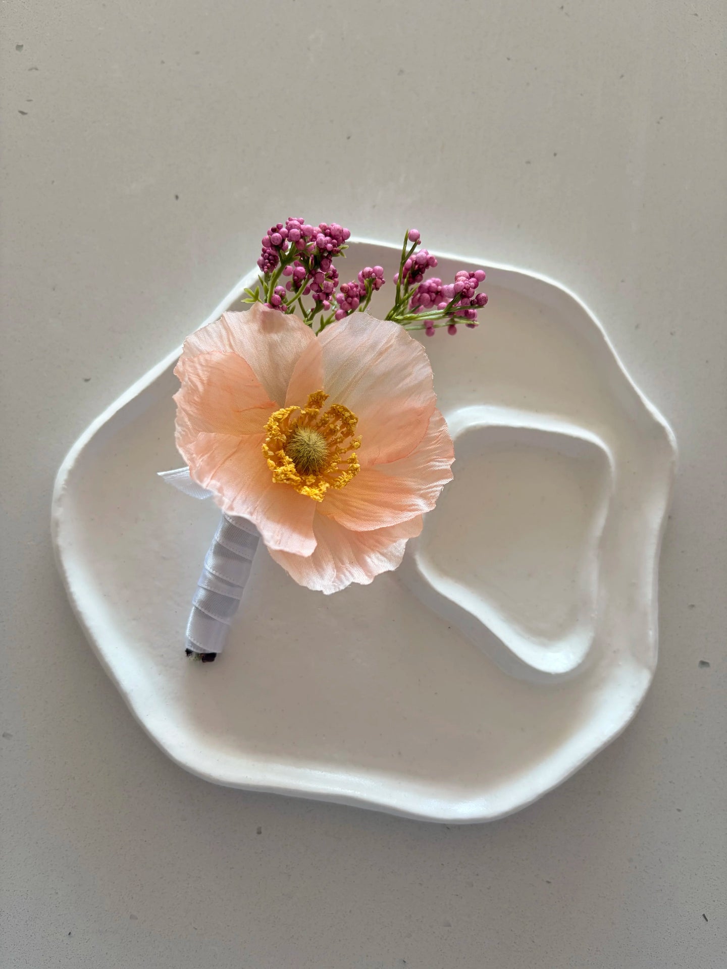 Peach poppy buttonhole on a a small white sculpted plate