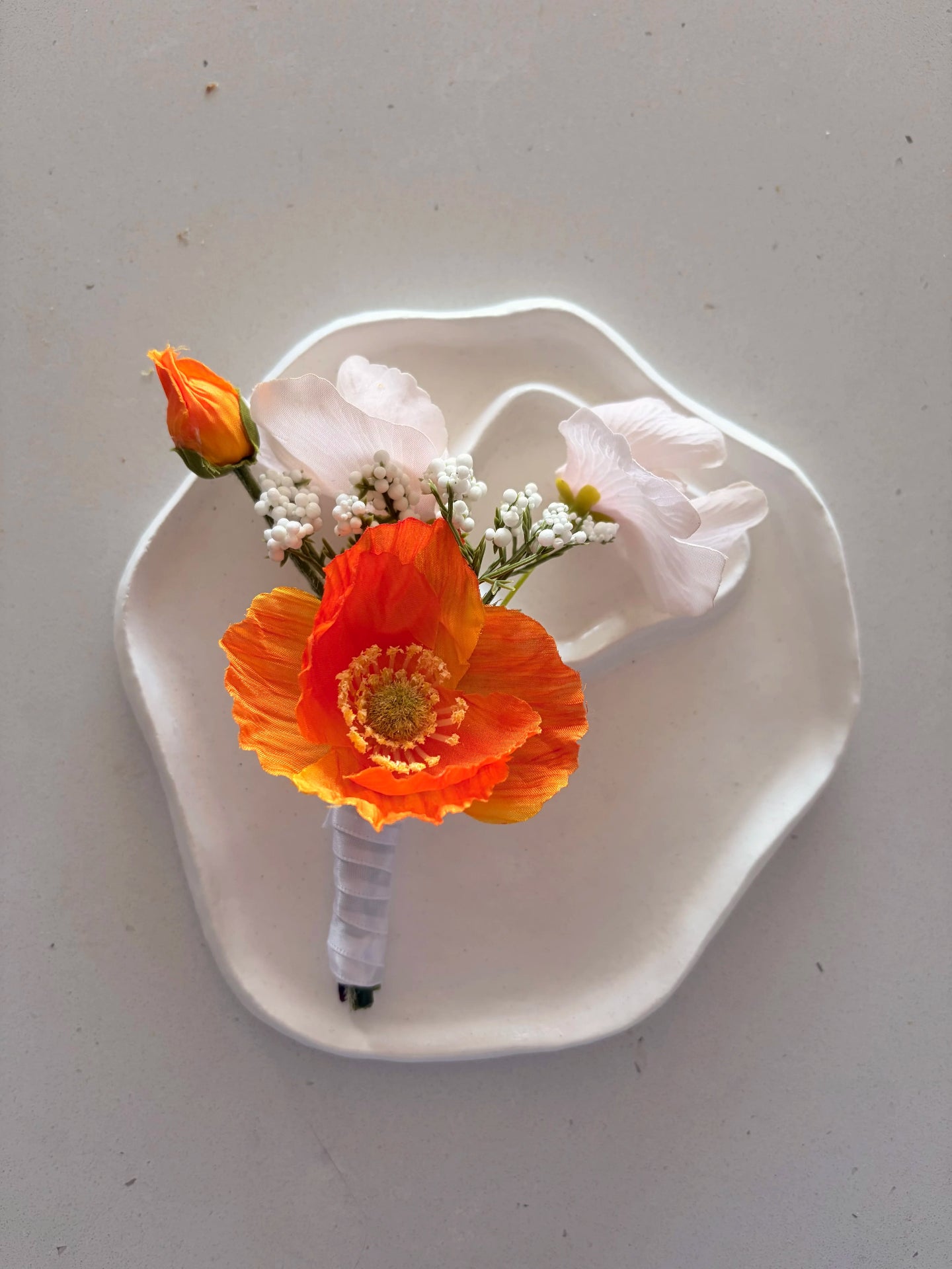 Orange poppy buttonhole on a a small white sculpted plate