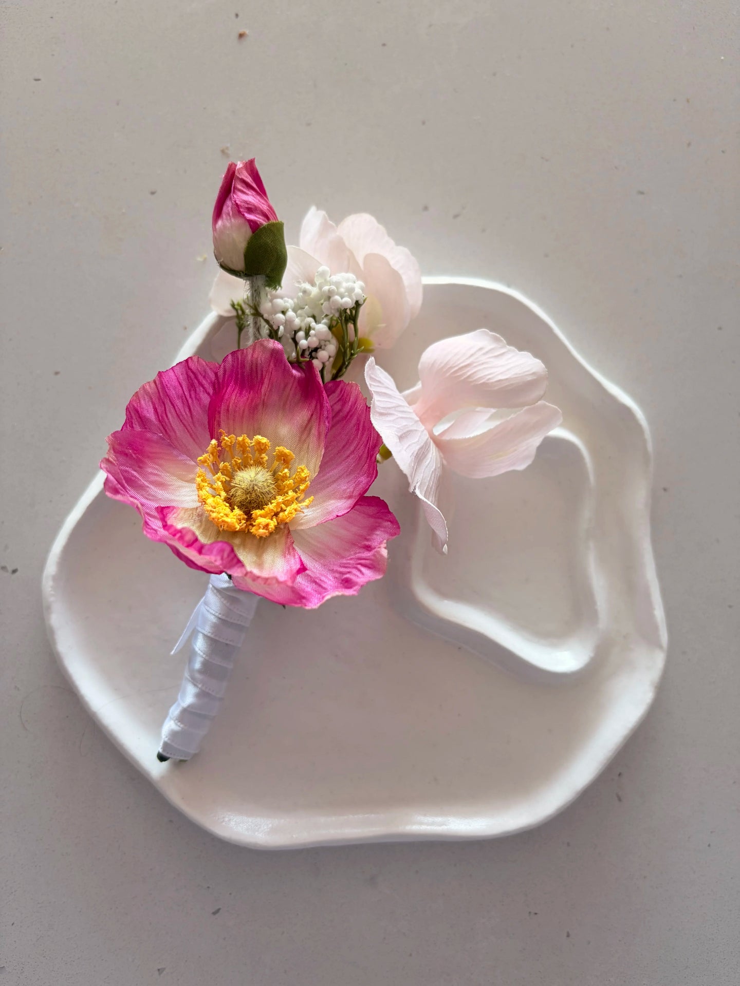 Pink poppy buttonhole on a a small white sculpted plate