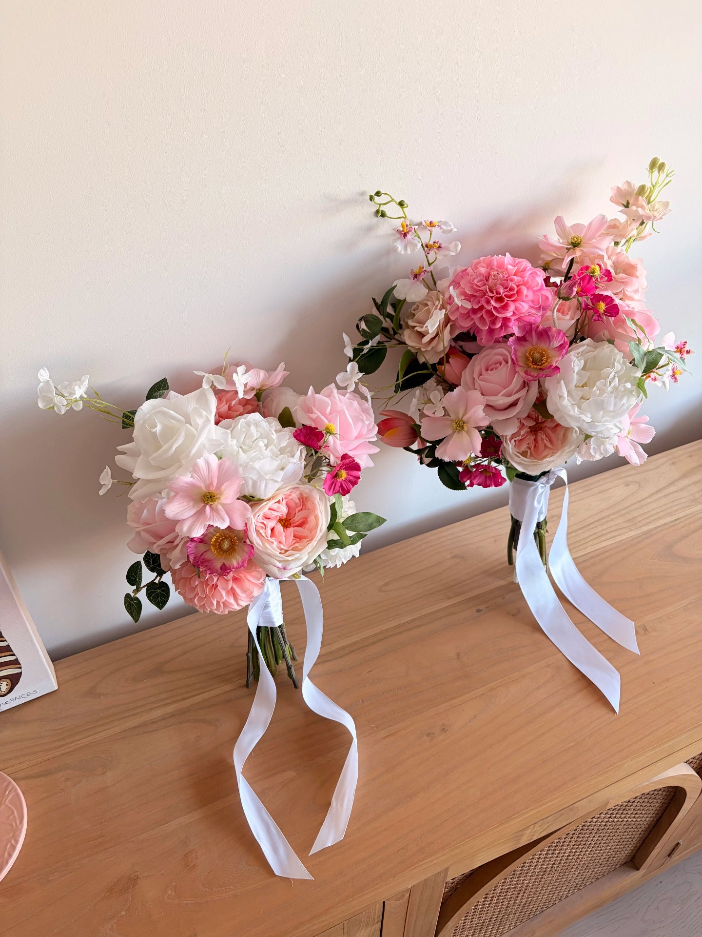 Two artificial wedding bouquets in different sizes leaning against a white wall