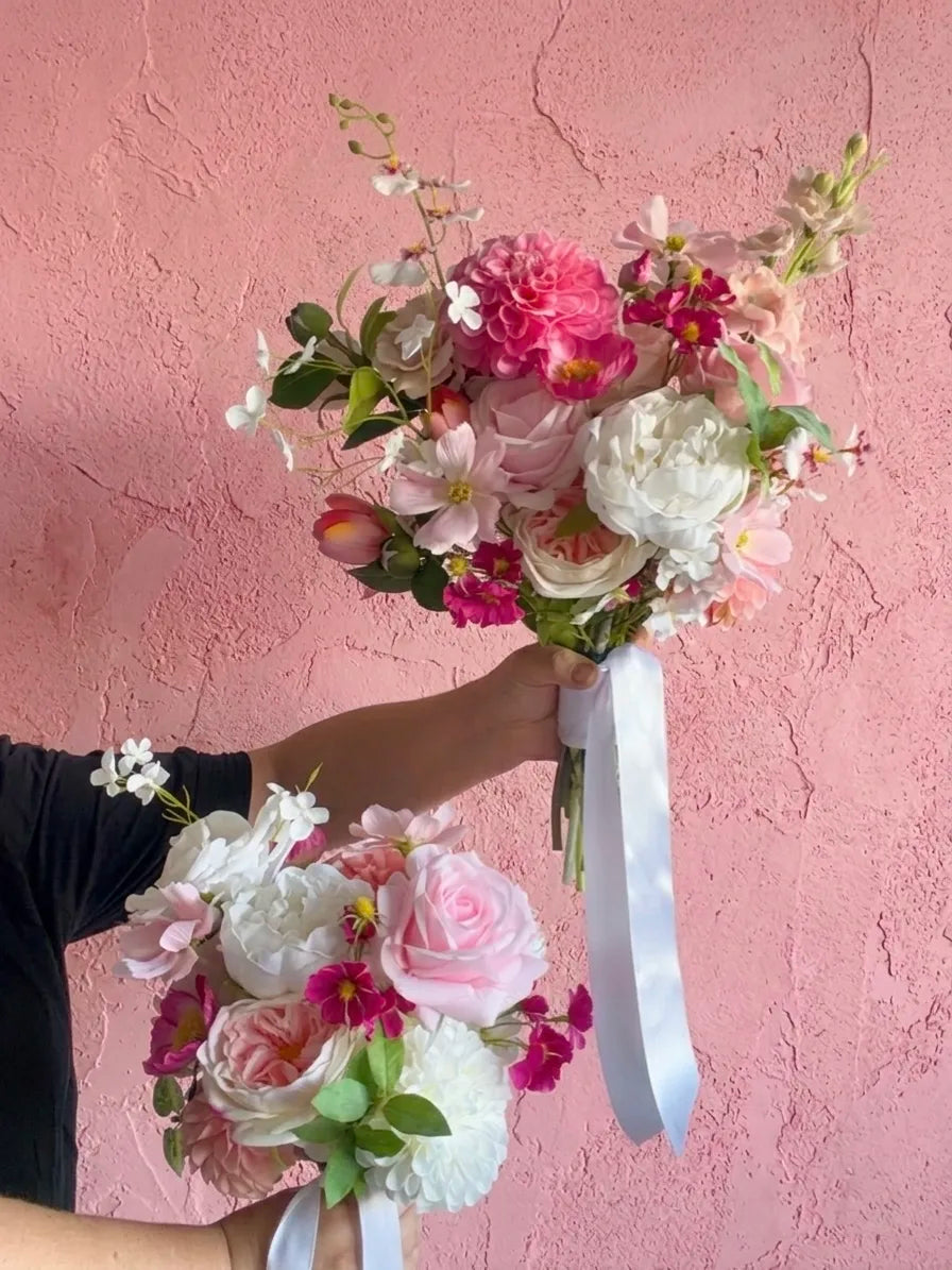 Two pink and white bouquets being held by hands with a pink textured wall in the background