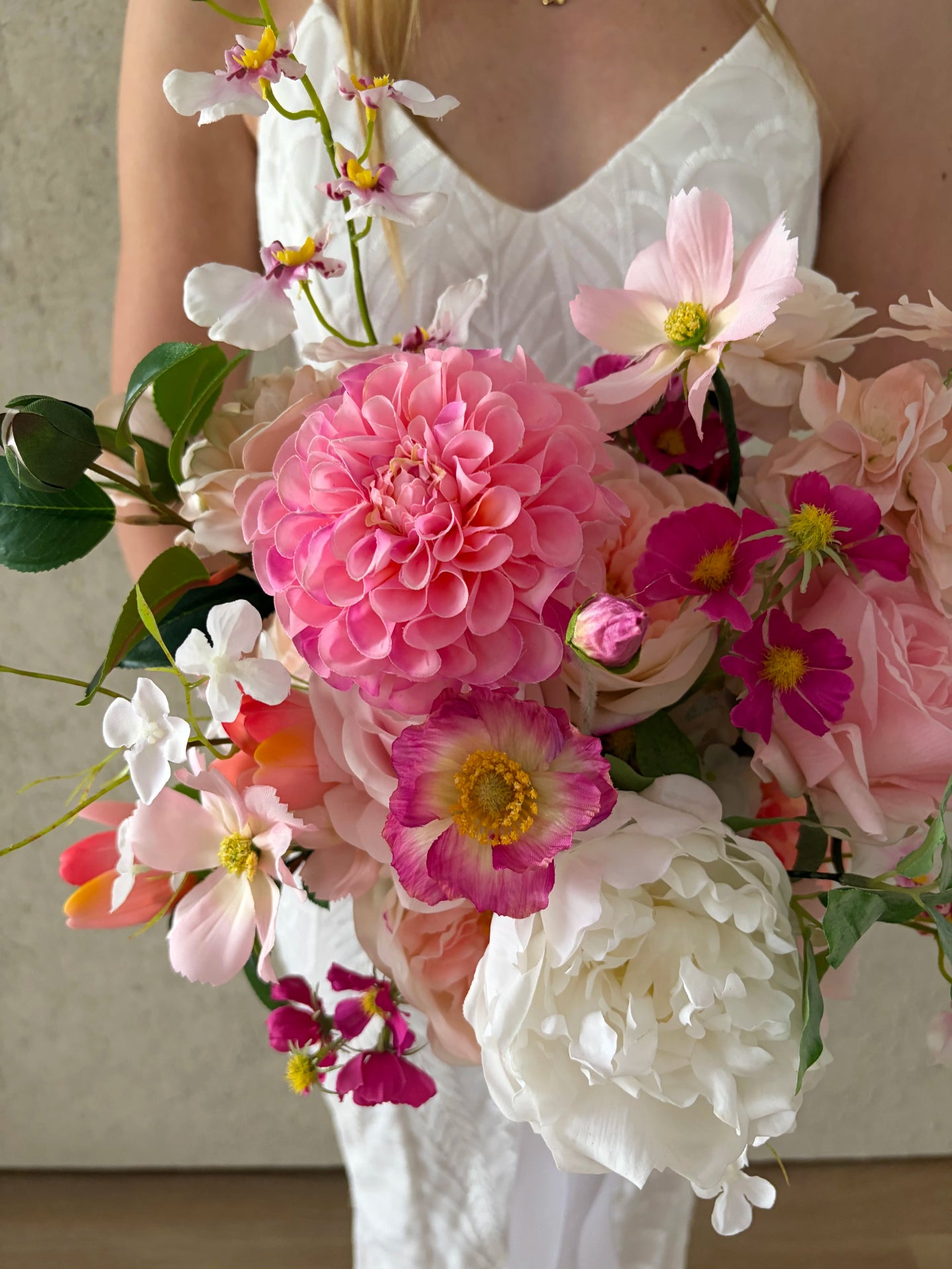 Artificial wedding  bouquet of pink and flowers held by a person wearing a white dress.