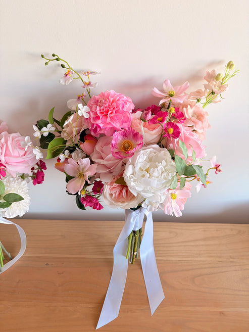 Garden style artificial wedding bouquet in pink and white against a white wallk