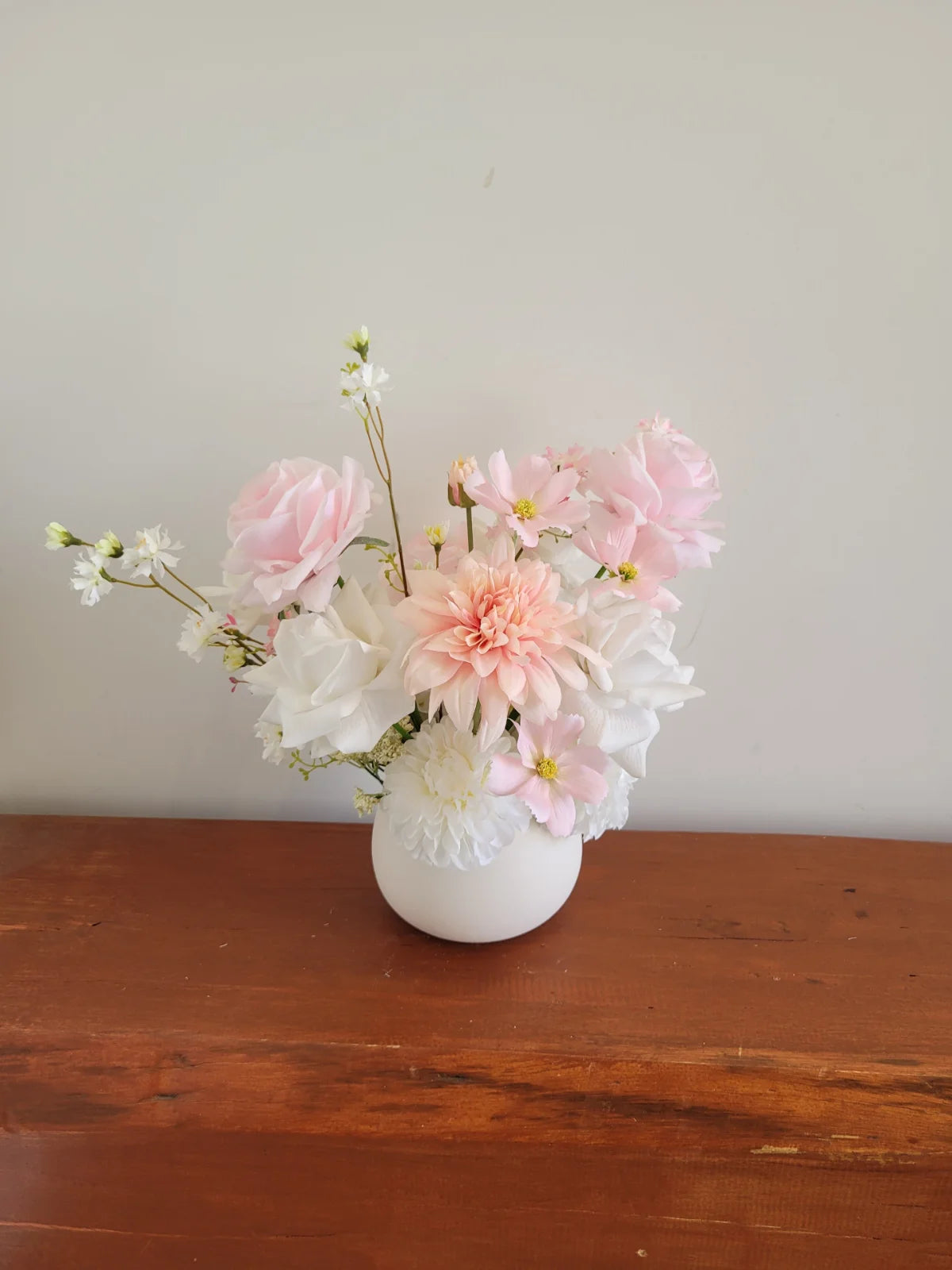 Bouquet of pink and white flowers in a white vase on a wooden surface with a light gray background