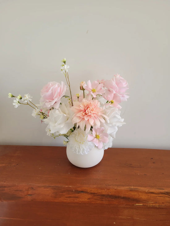 Bouquet of pink and white flowers in a white vase on a wooden surface with a light gray background