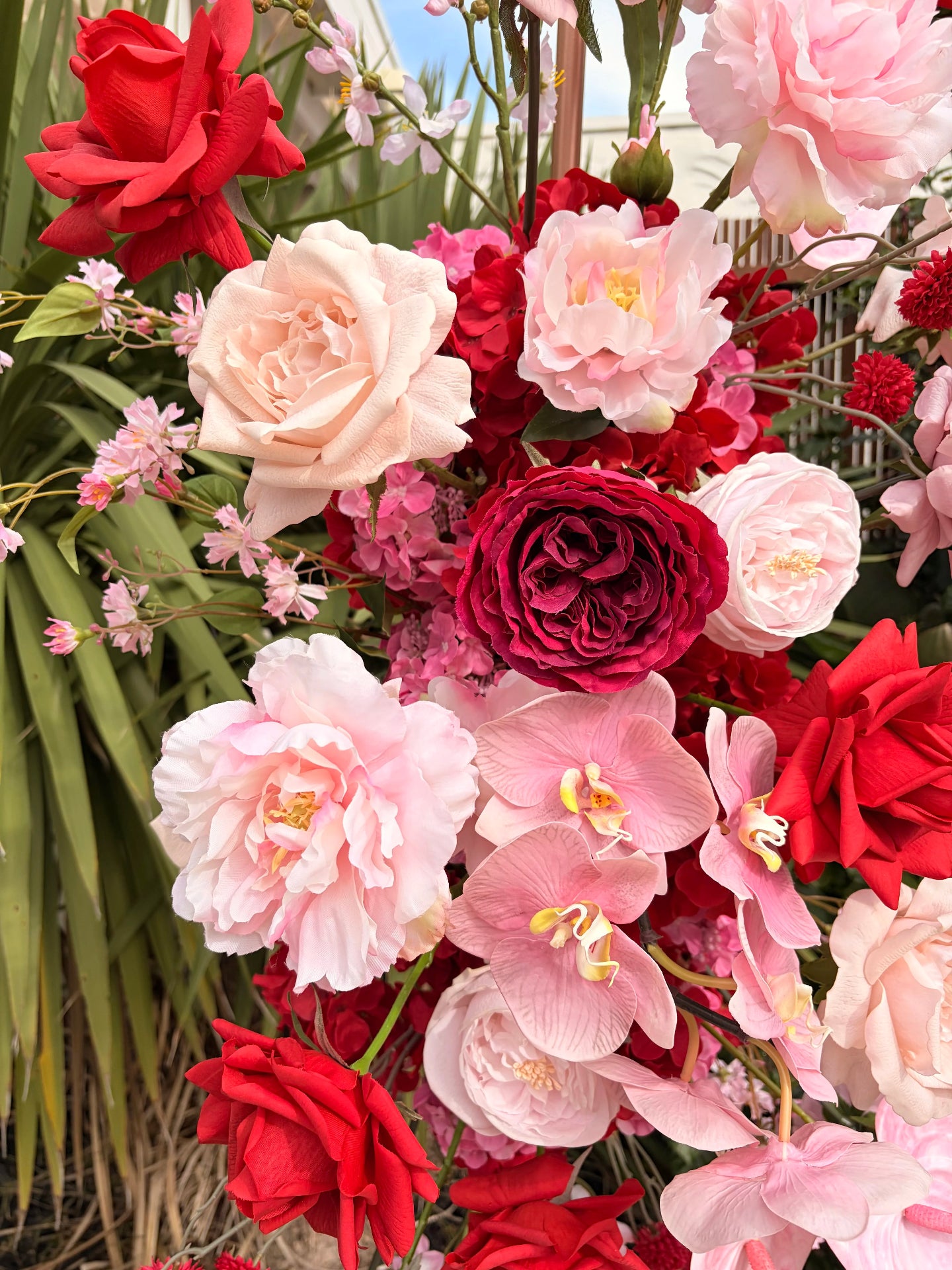 Close up of red, pink, and white faux flowers with greenery in the background