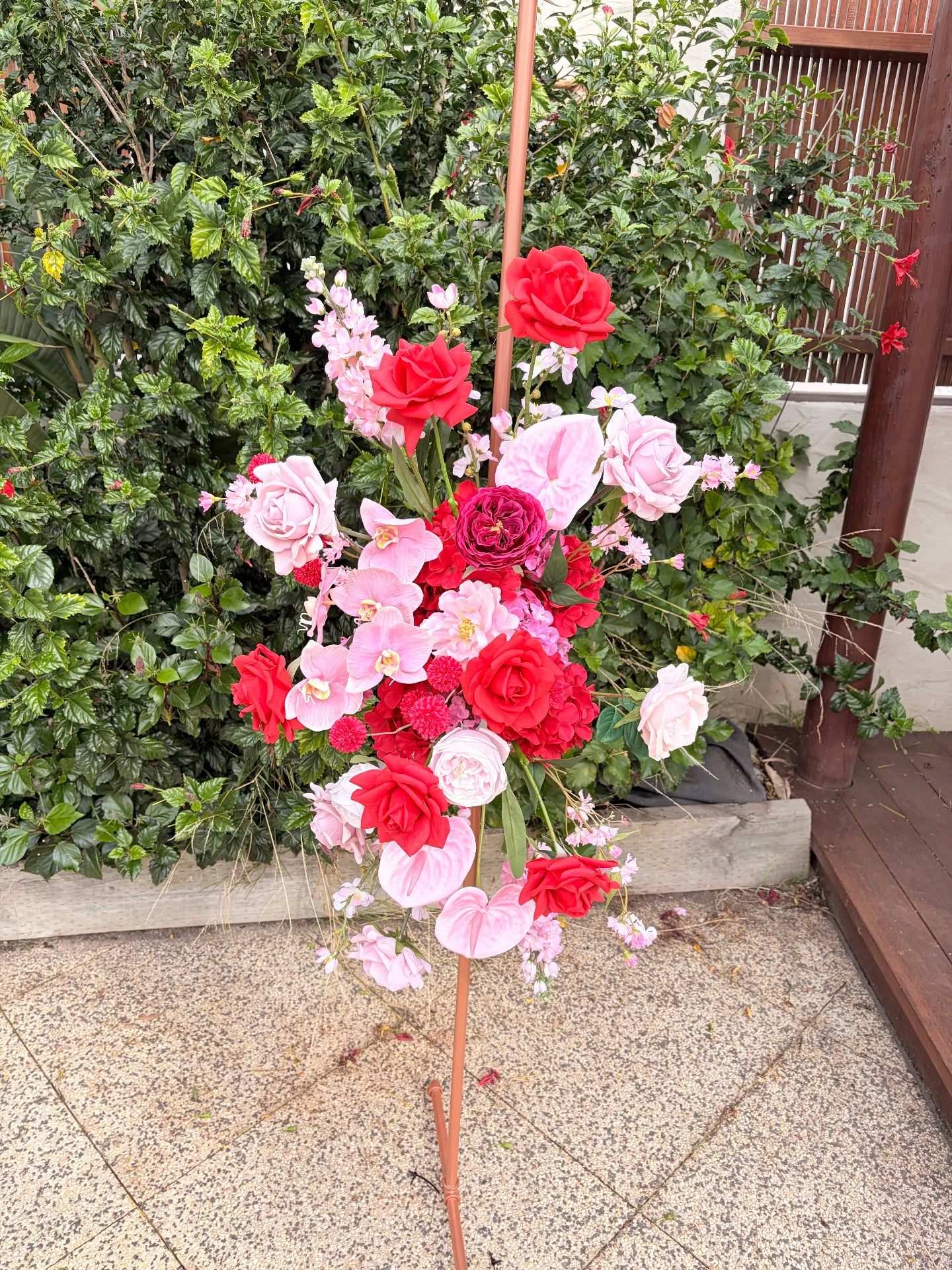 Arbour floral arrangement with red, pink, and white flowers on a stand outdoors.