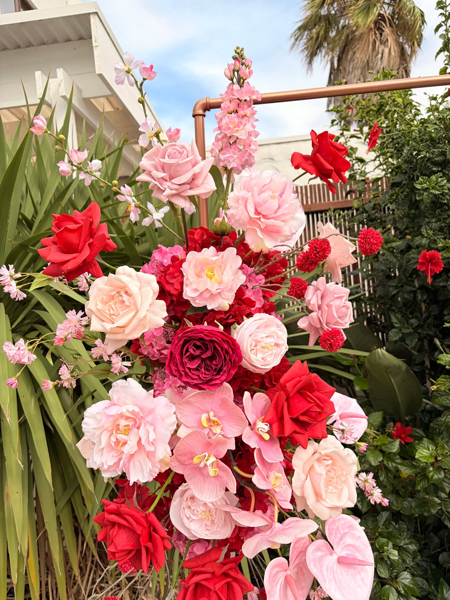 Close up of red and pink artificial flowers with greenery and a blue sky