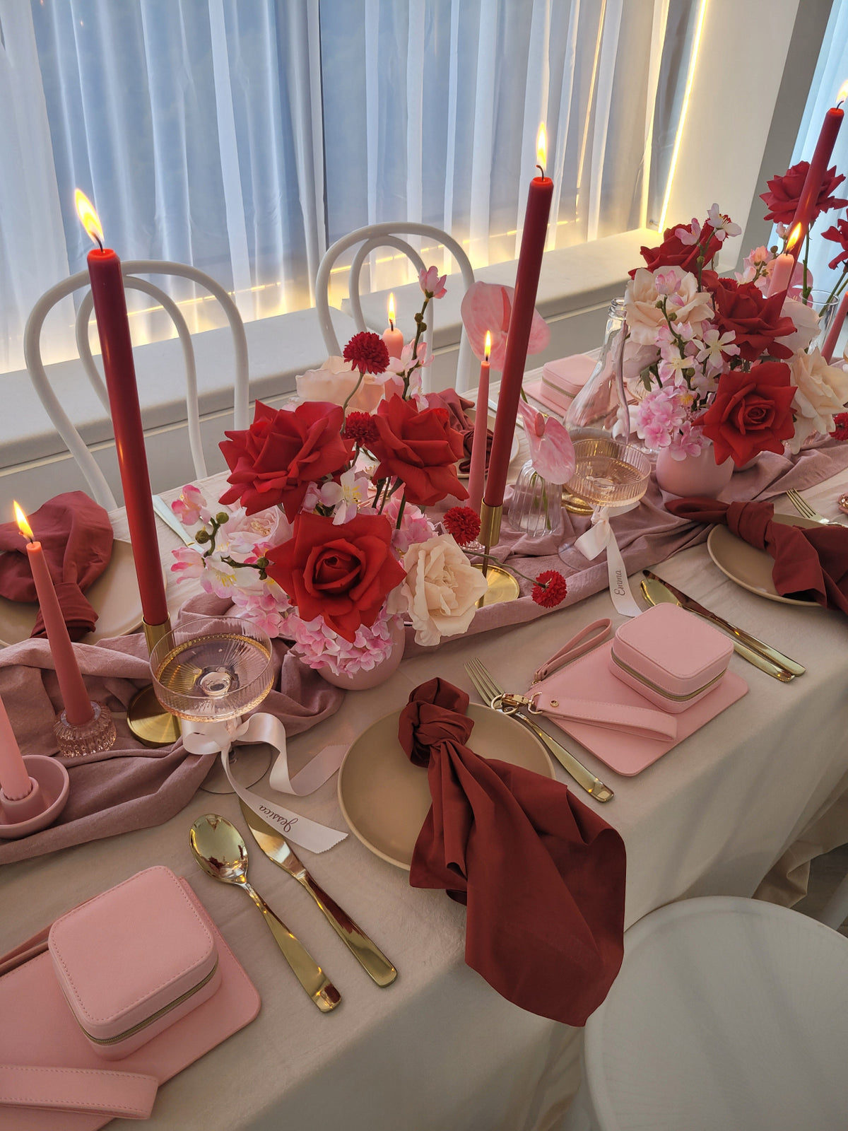 Decorative table setting with red and pink flowers, candles, and cutlery.
