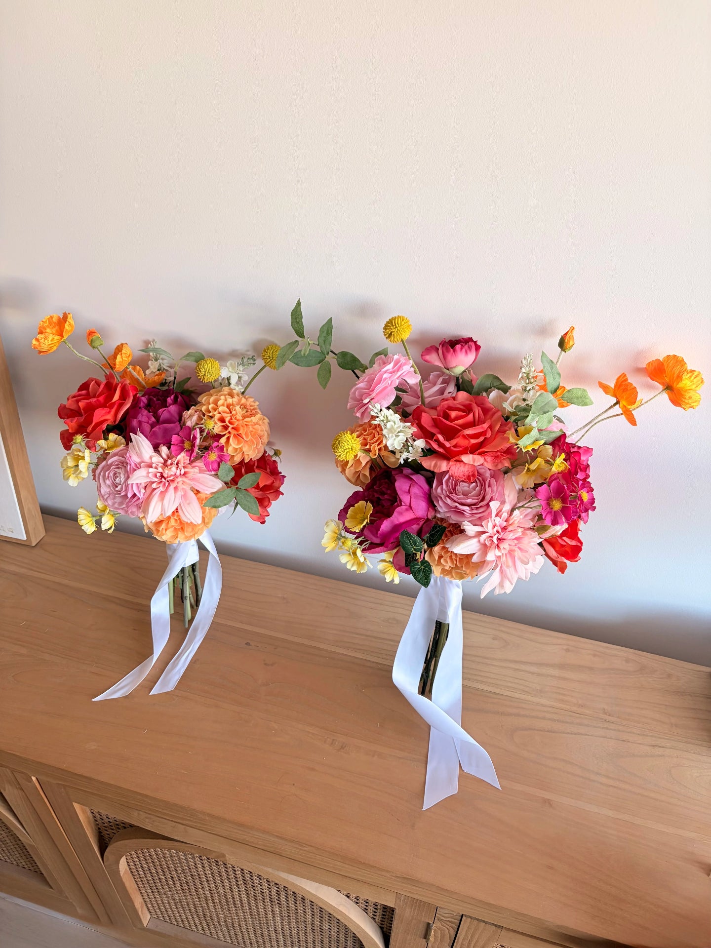 Two bright wedding bouquets in fuchsia, orange and pink on a wooden cabinet in front of a white wall