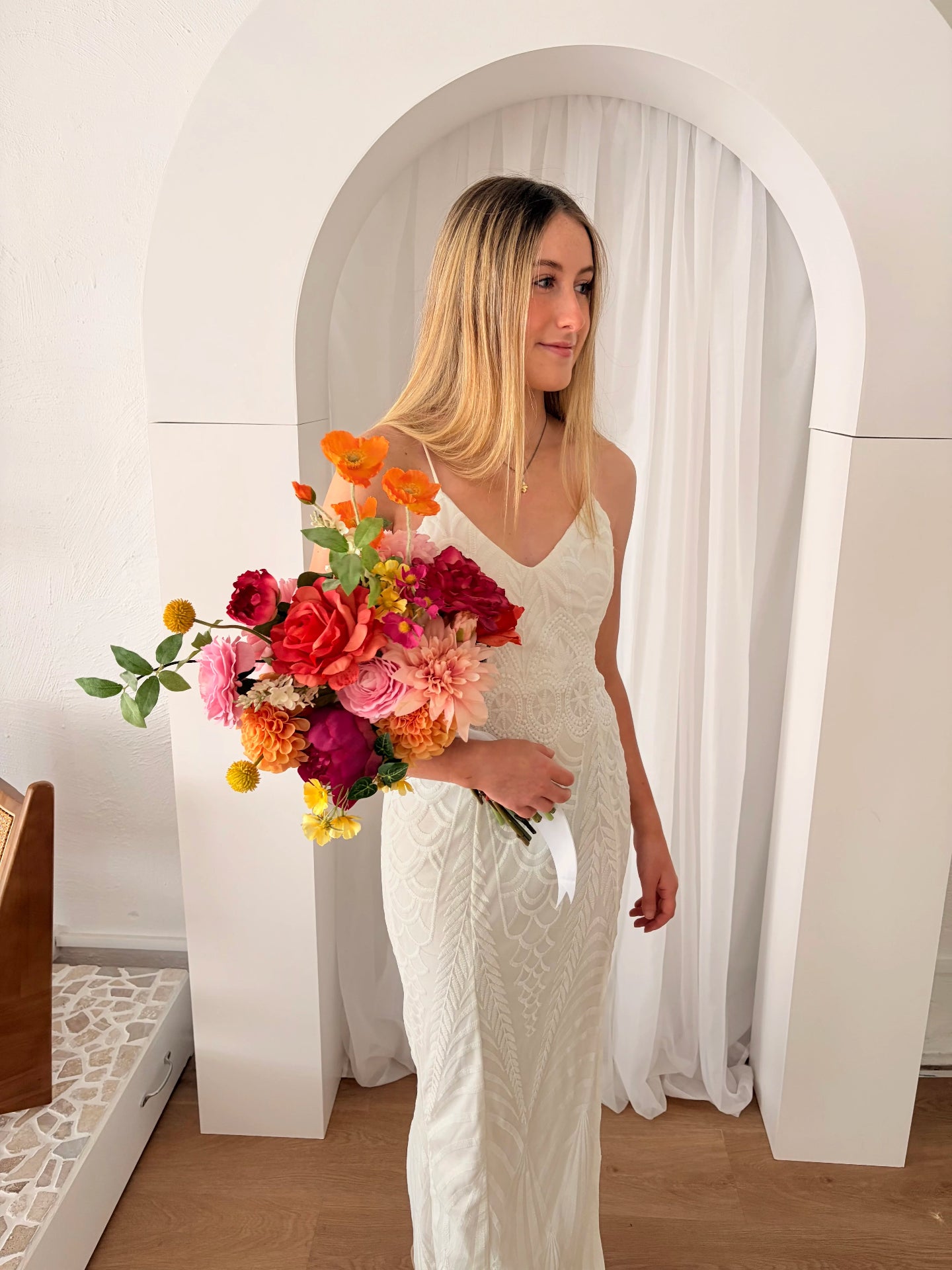 Woman in a white dress holding a bouquet of faux flowers in a bright room.