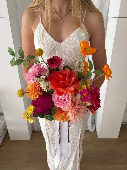 Woman holding a colourful bouquet of artificial flowers in a white room.