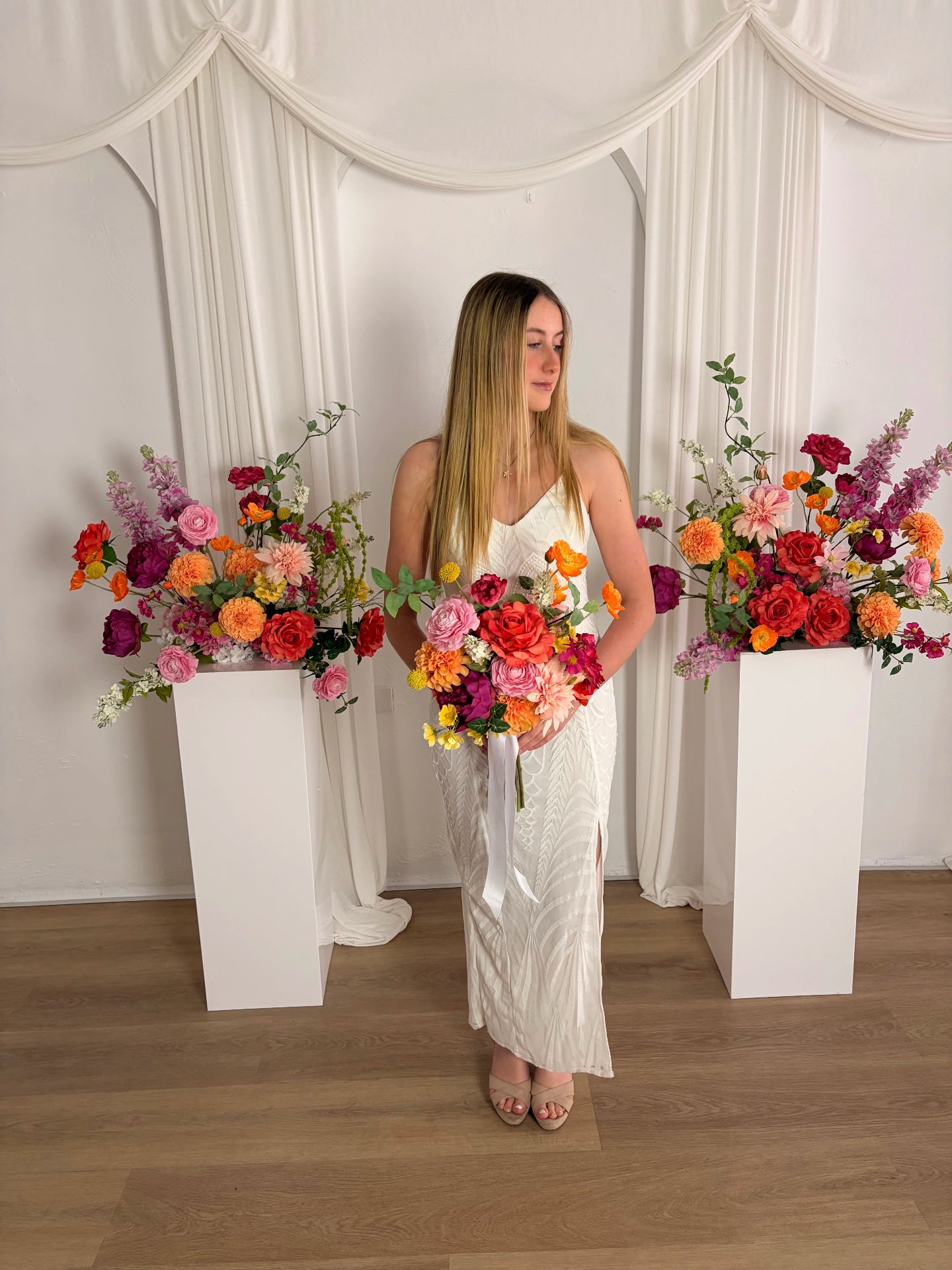 Women holding a bright artificial wedding bouquet in front of pedestals with bright flowers