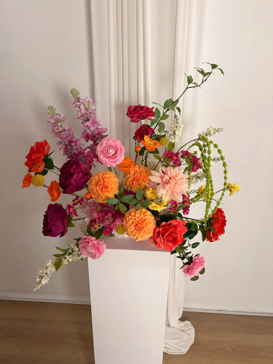 Bright and whimsical artificial flower arrangement on a wedding plinth with central dahlias