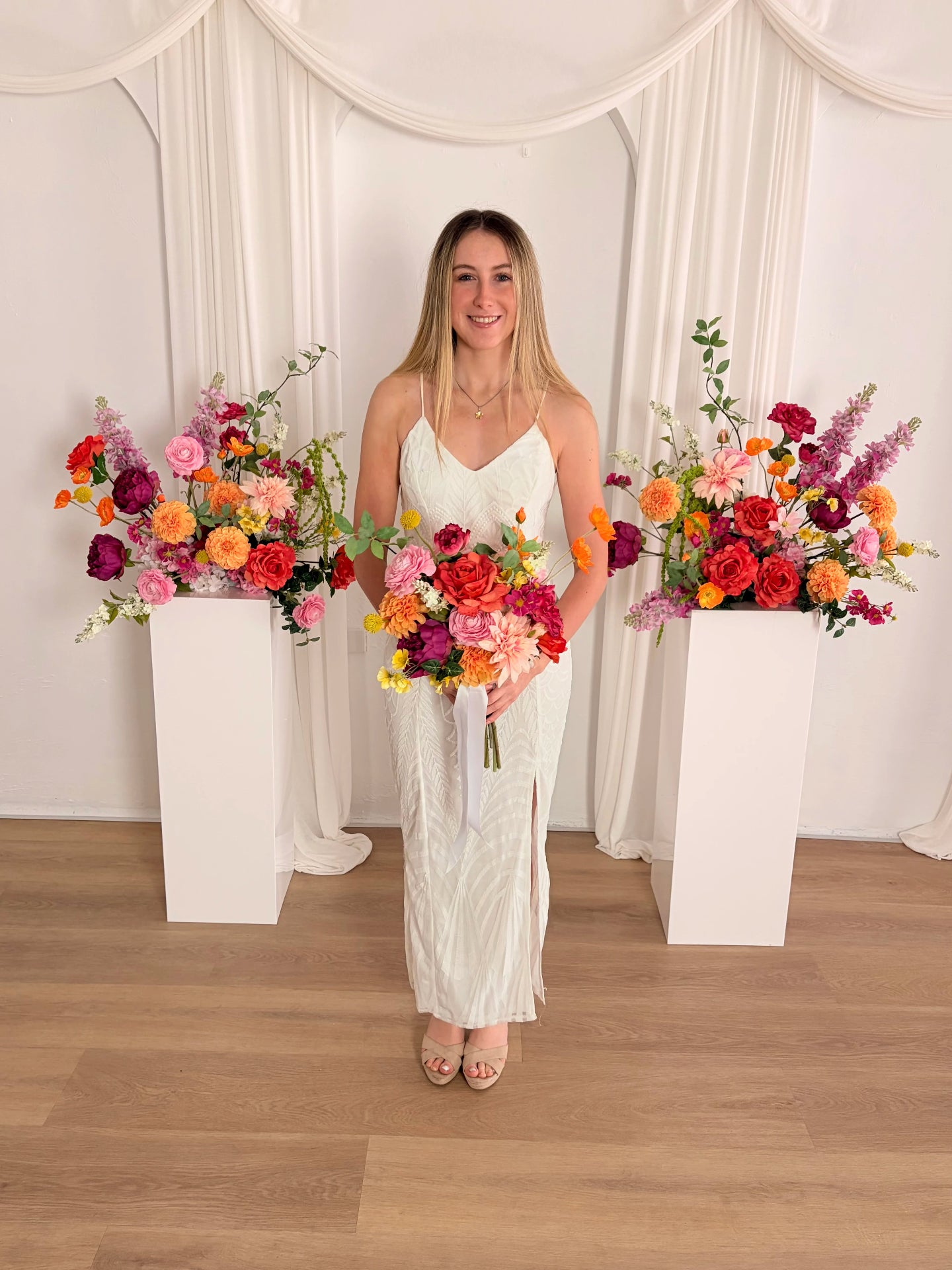 Women holding an artificial wedding bouquet in front of two pillars with matching flower arrangements