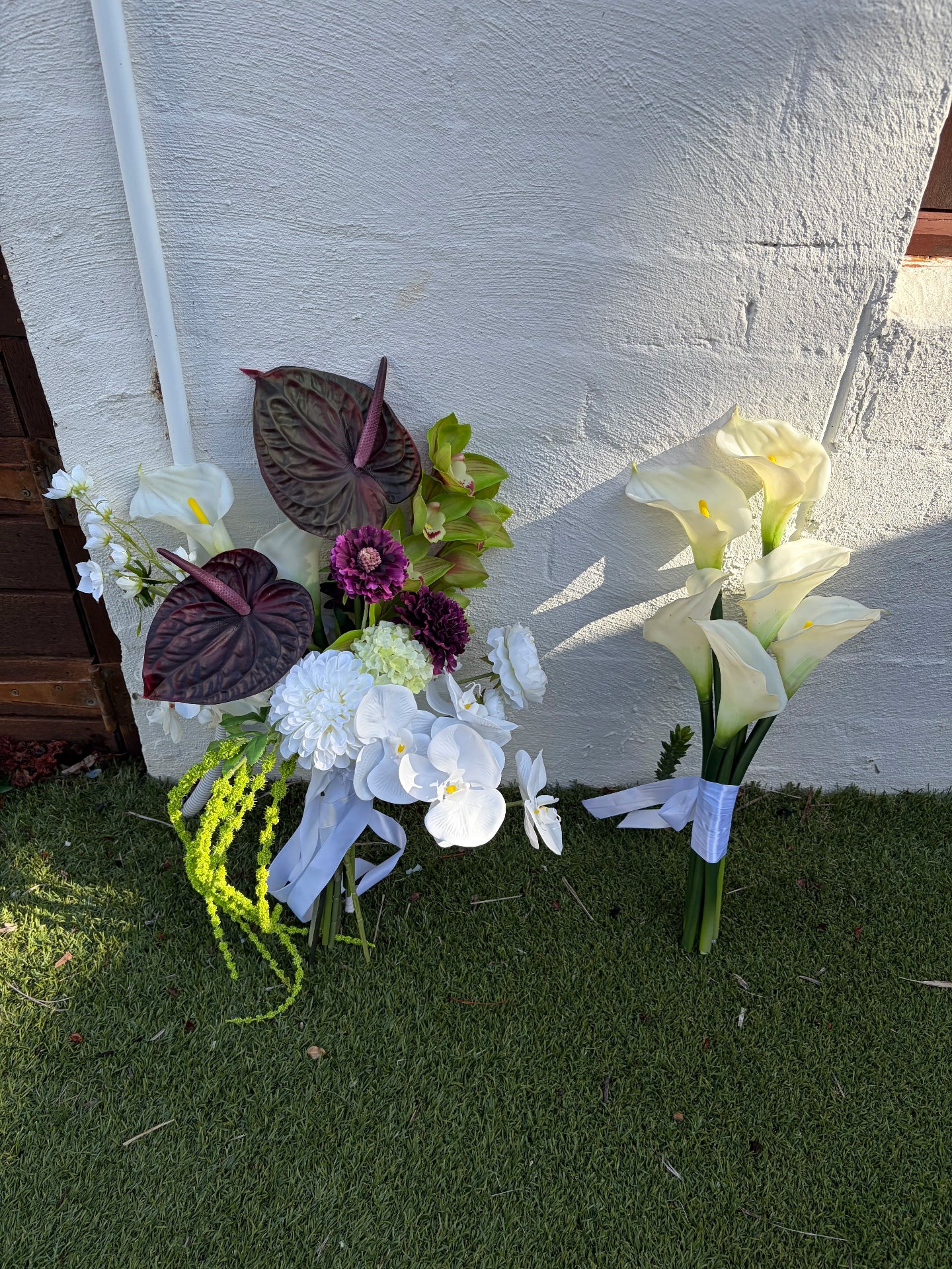 Bridal bouquet with burgundy anthuriums next to a calla lily bouquet against a white wall