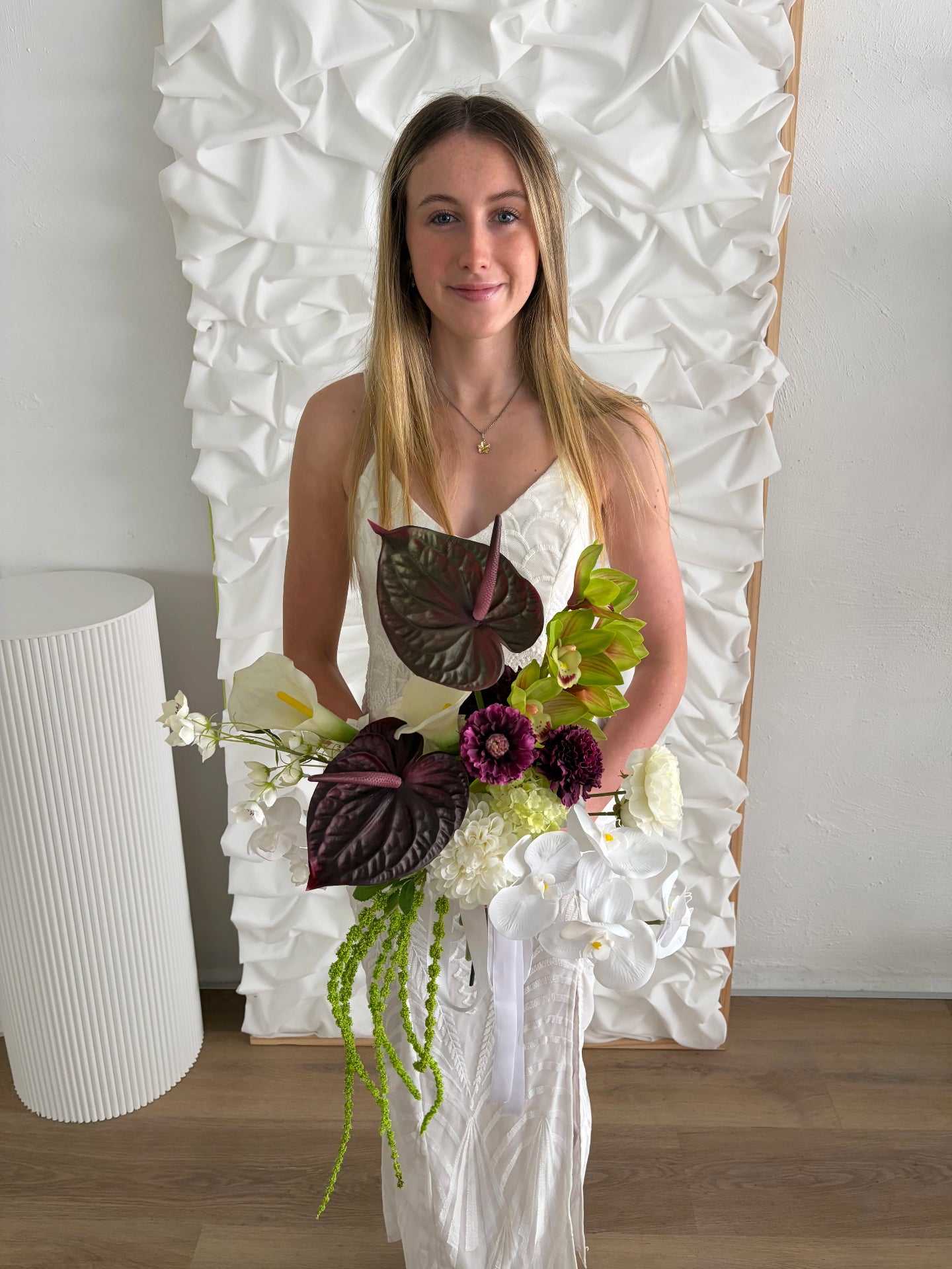 Woman holding a modern wedding bouquet of flowers in front of a textured white wall.
