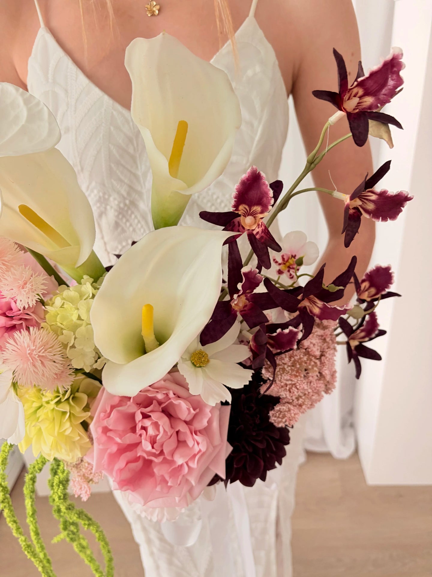 Bouquet of flowers with white calla lilies, pink carnations, and dark purple orchids held by a person in a white dress.
