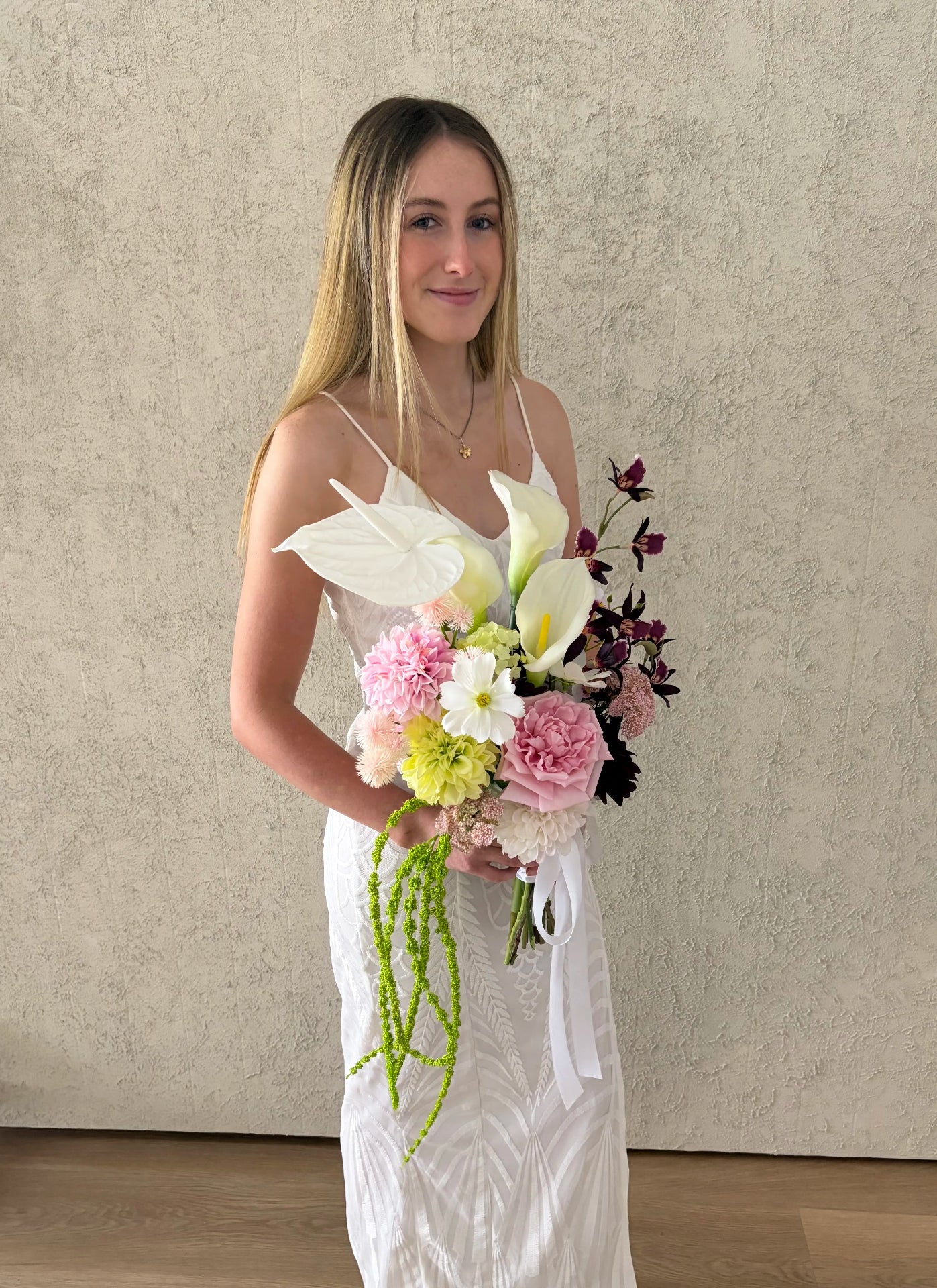 Woman in a white dress holding a sculptural bouquet of flowers with calla lilies against a plain background