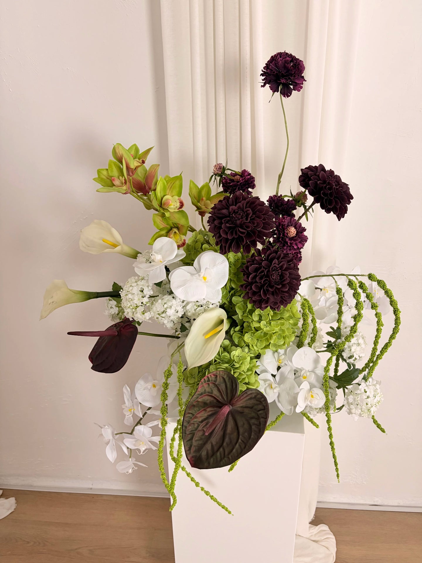 Sculptural artificial flower arrangement in green, burgundy and white colours on a white plinth in a white room