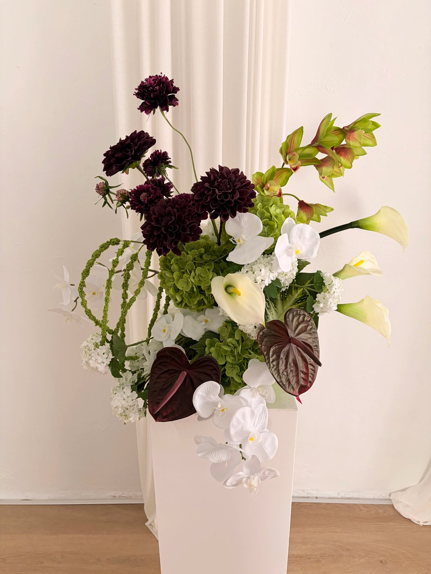 Architectural artificial flower arrangement in green, burgundy and white colours on a white plinth