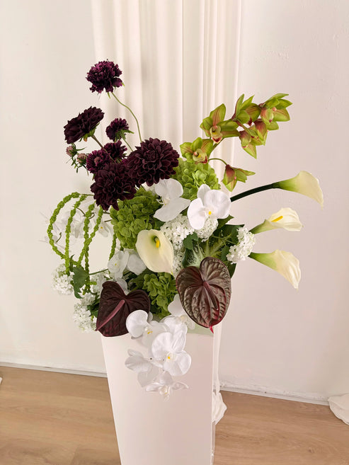 Sculptural artificial flower arrangement in green, burgundy and white colours on a white plinth