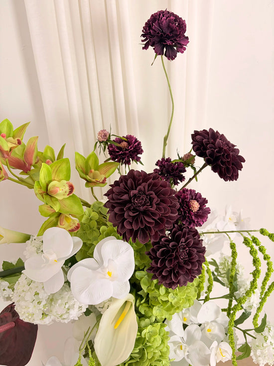 Close up of burgundy dahlias that form part of a sculptural artificial flower arrangement