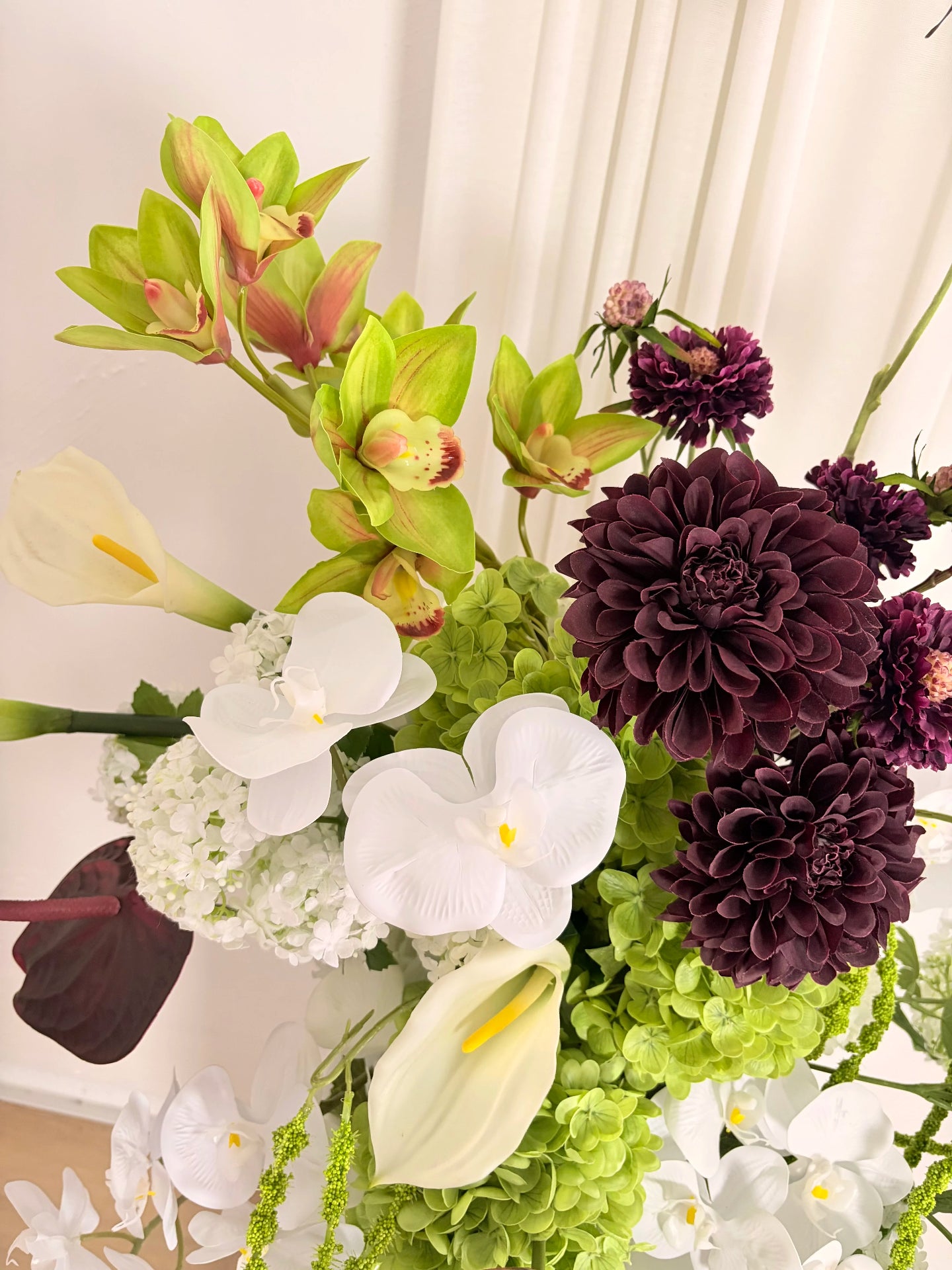 Close up of an artificial flower arrangement with a green cymbidium orchids and burgundy dahlias