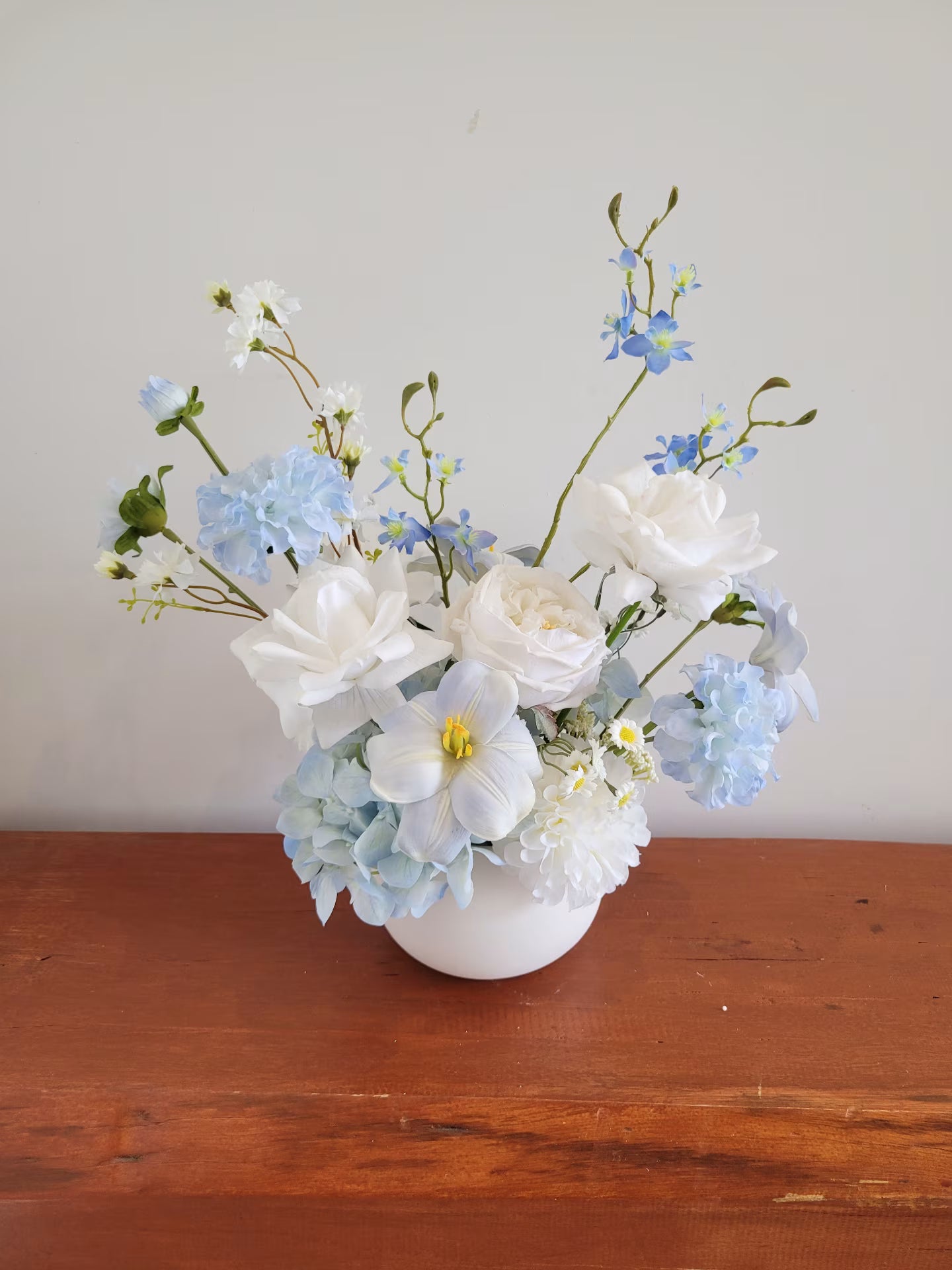 Light blue and white flower arrangement on a wooden bench against a white wall