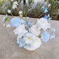 Light blue and white flower arrangement on a concrete bench outdoors