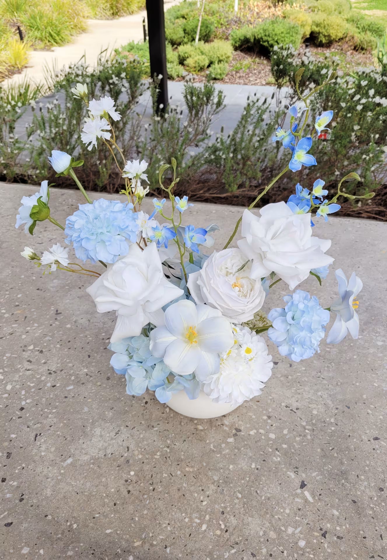 Light blue and white flower arrangement on a concrete bench outdoors