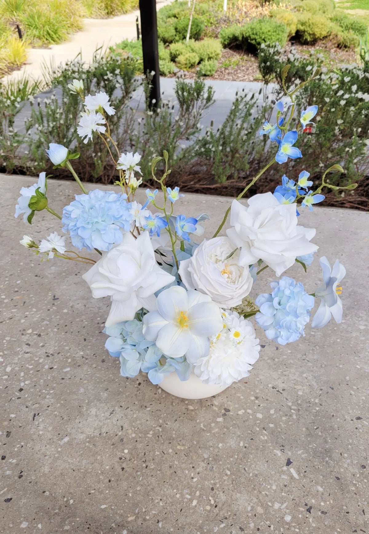 Floral arrangement with white and light blue flowers on a concrete surface