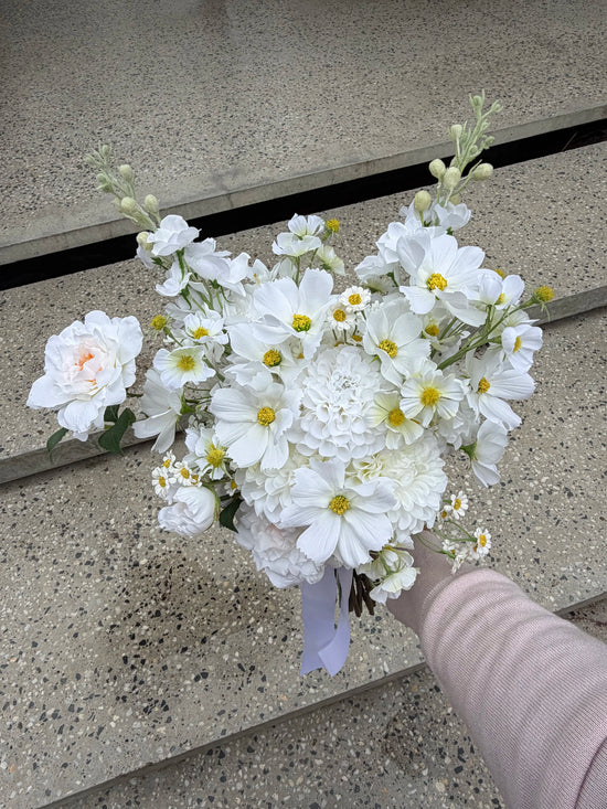 Artificial wedding bouquet of white cosmos and dahlias against textured concrete steps