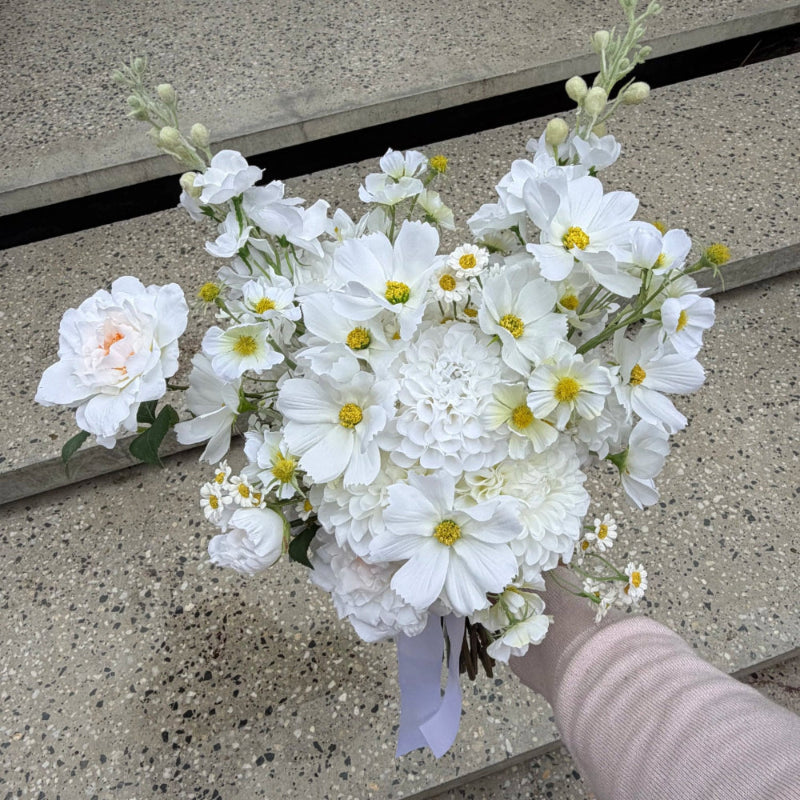 White wedding bouquet of artificial flowers held by a person against concrete steps