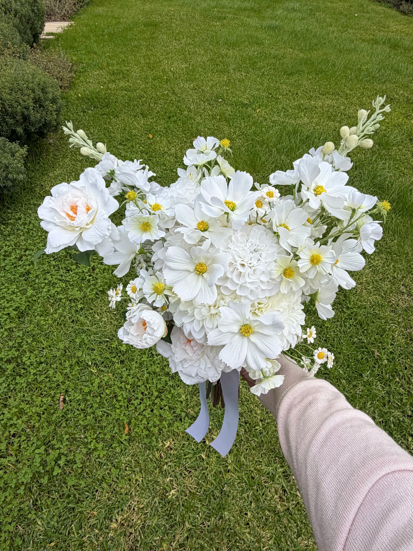 Wedding bouquet of white flowers held by a person on a grassy background
