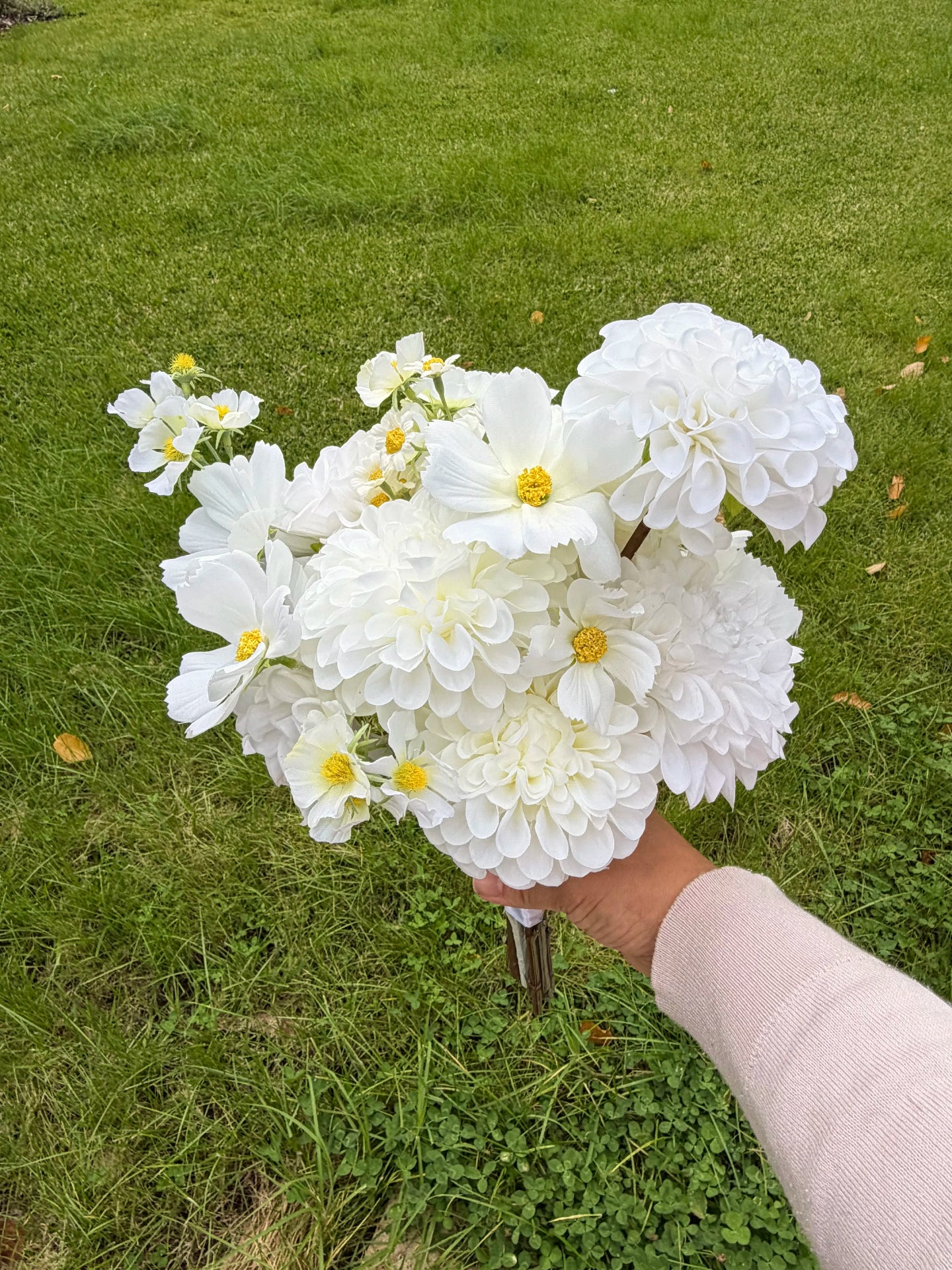 Bridesmaid bouquet of white flowers held in front of a grassy background