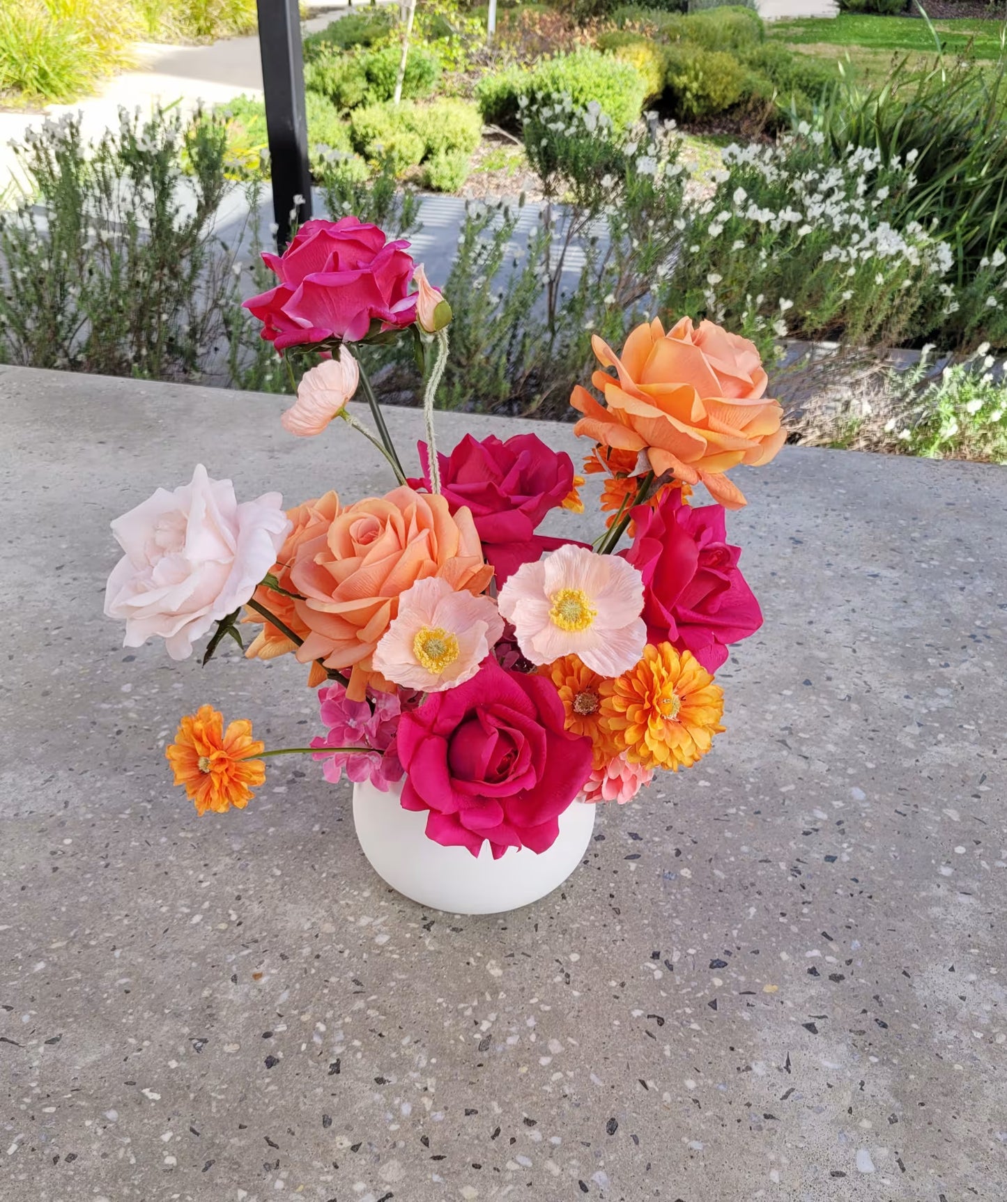 Hot pink and white faux flower arrangement on a concrete bench outside