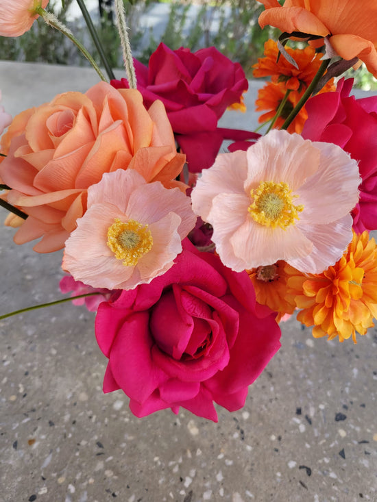 Close up of peach coloured poppies amongst hot pink and orange roses