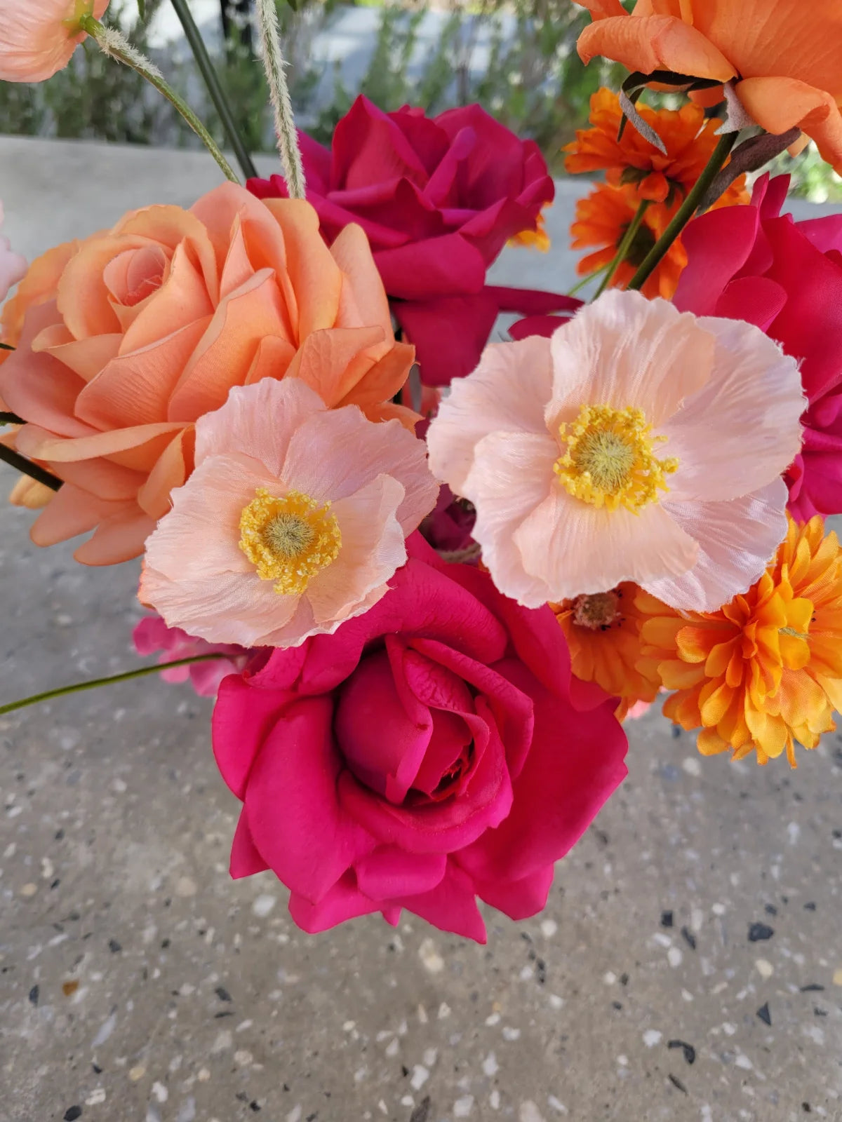 Colourful arrangement of flowers including roses and anemones on a concrete surface.