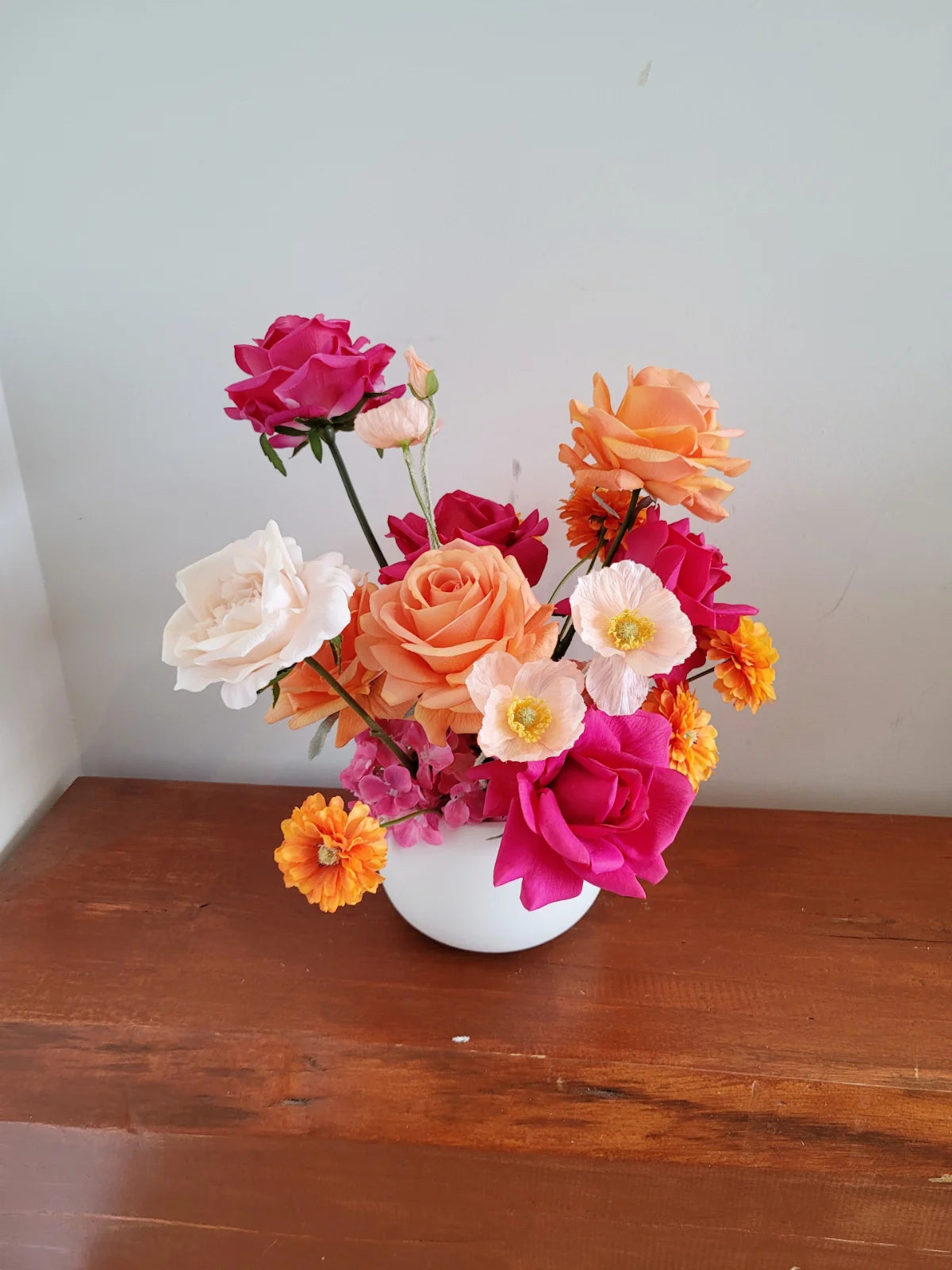Colourful flower arrangement in a white vase on a wooden surface with a white wall background