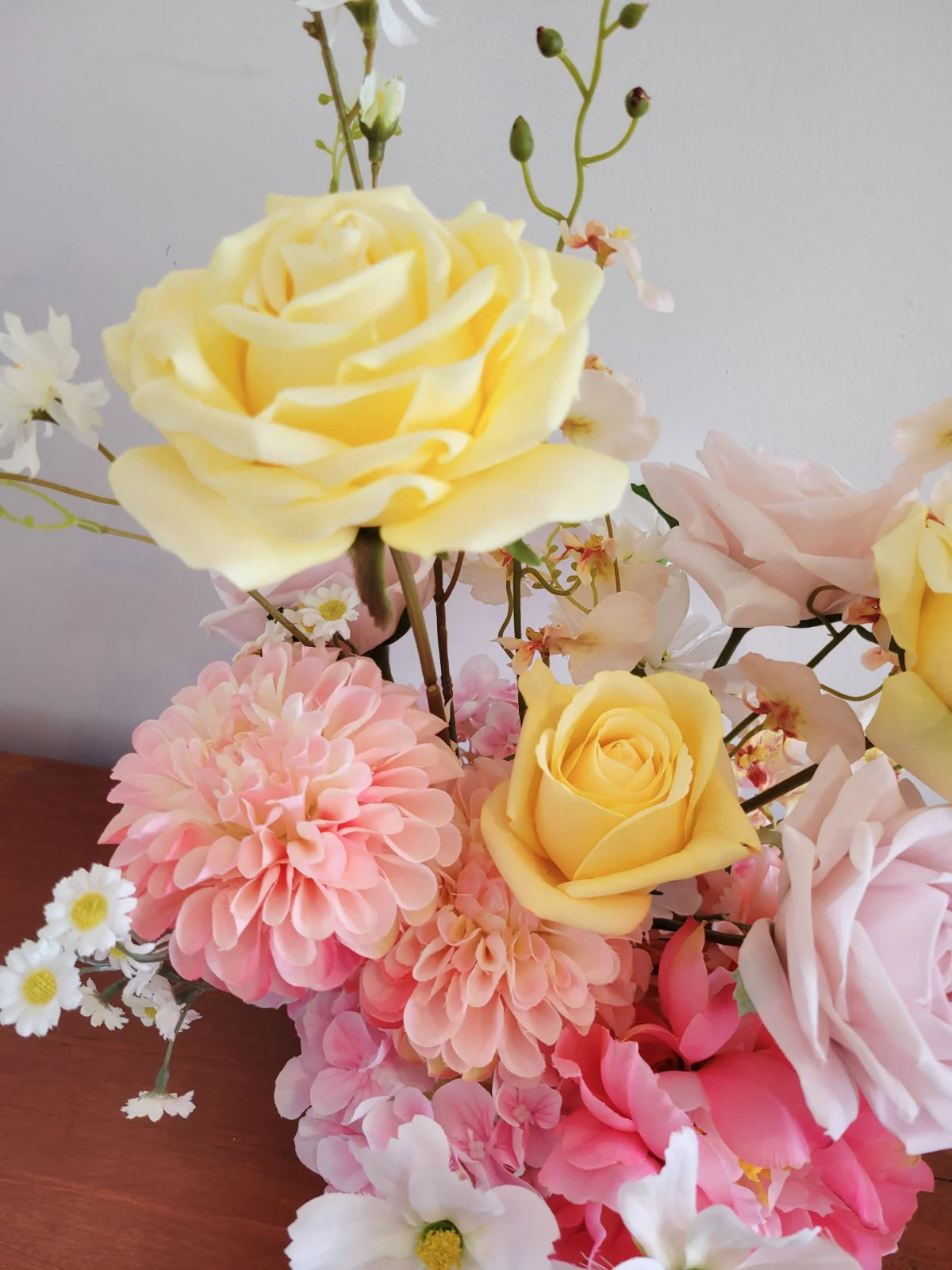 Bouquet of yellow, pink, and white flowers on a wooden surface with a light gray background.